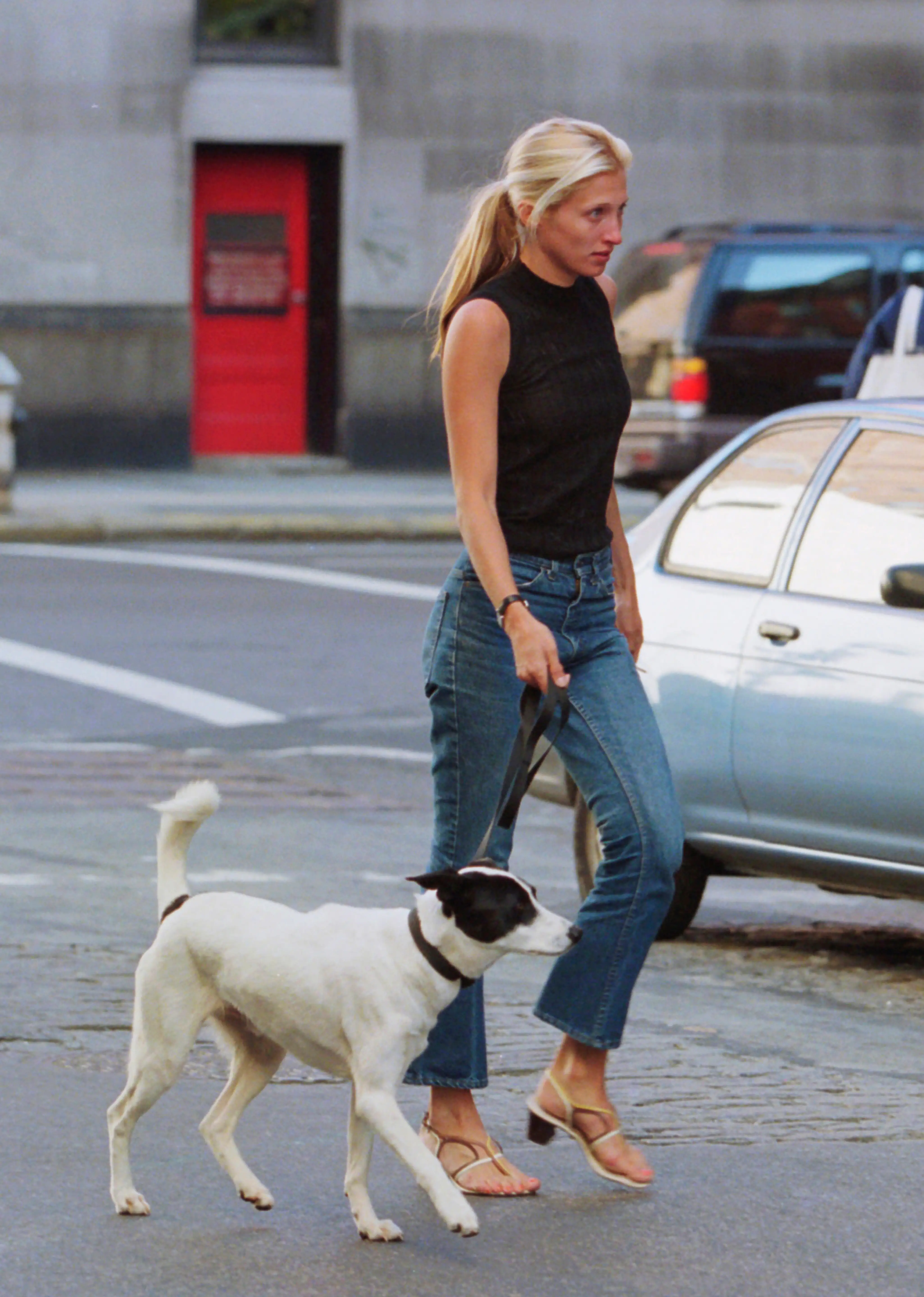Carolyn Bessette-Kennedy wearing jeans and a black top walking her dog in New York City in 1996