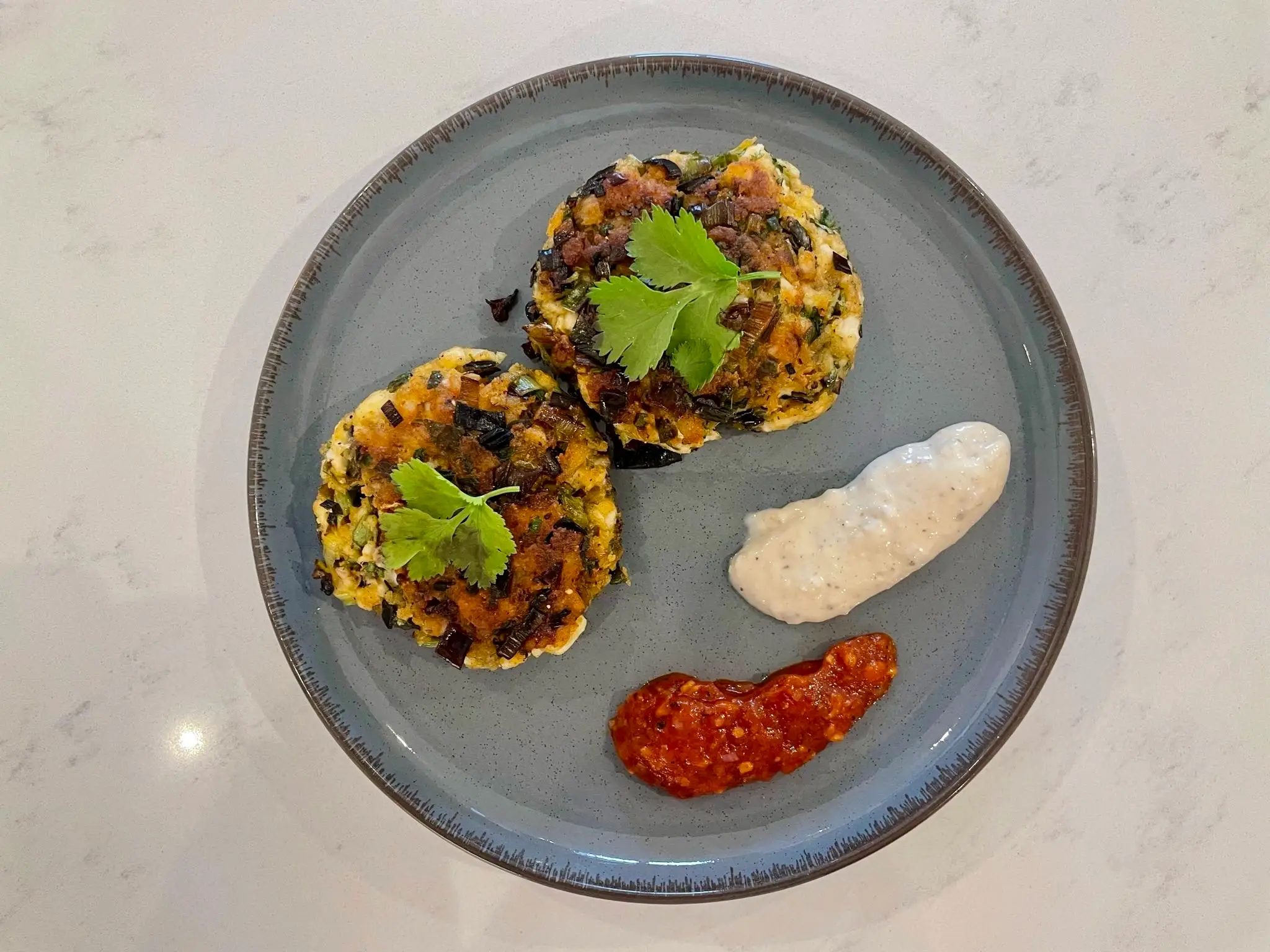 Fishcakes on plate with garnish and garlic mayo and salsa on the side.
