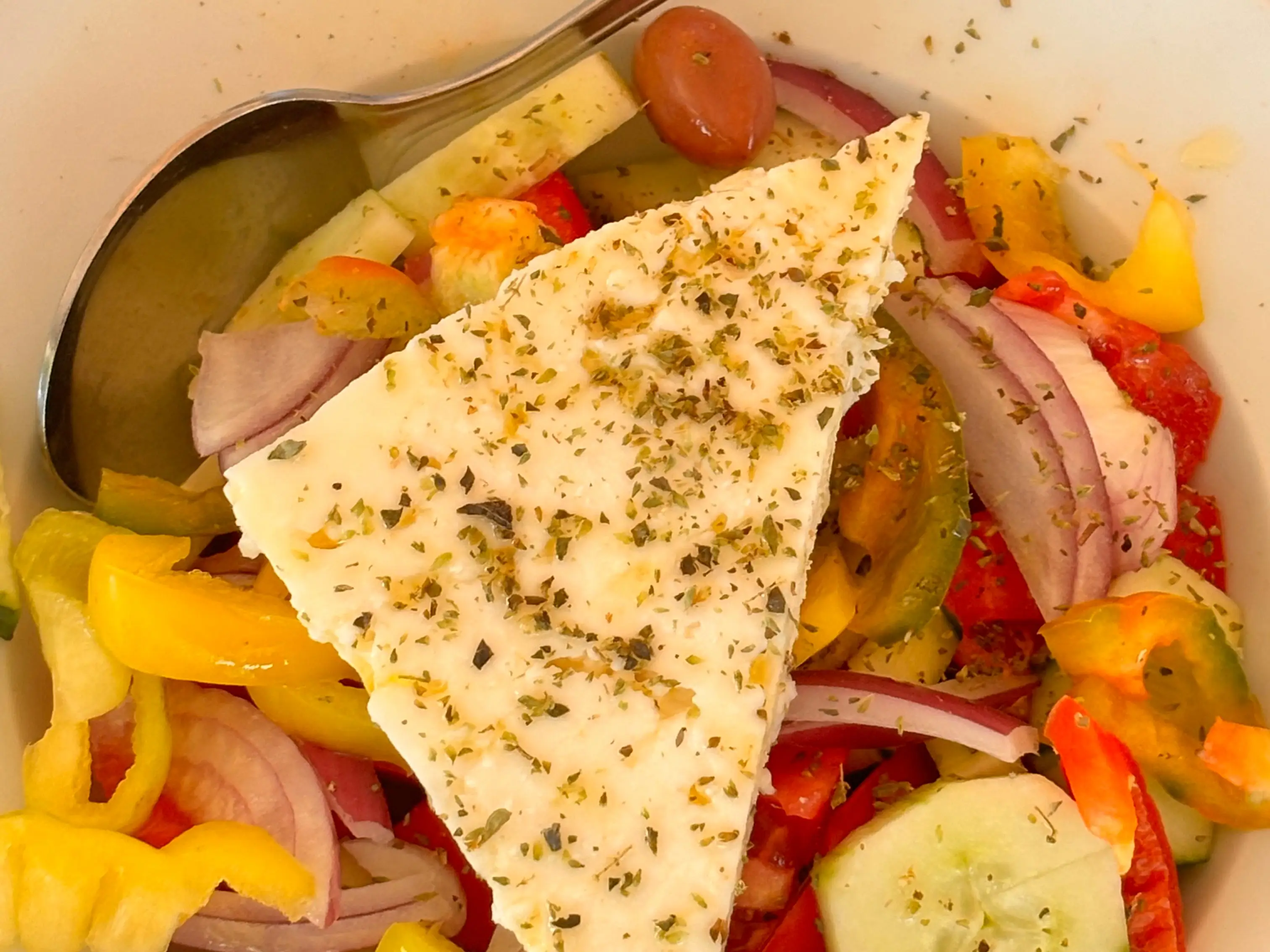 A close-up of a Greek salad with veggies, feta, and herbs