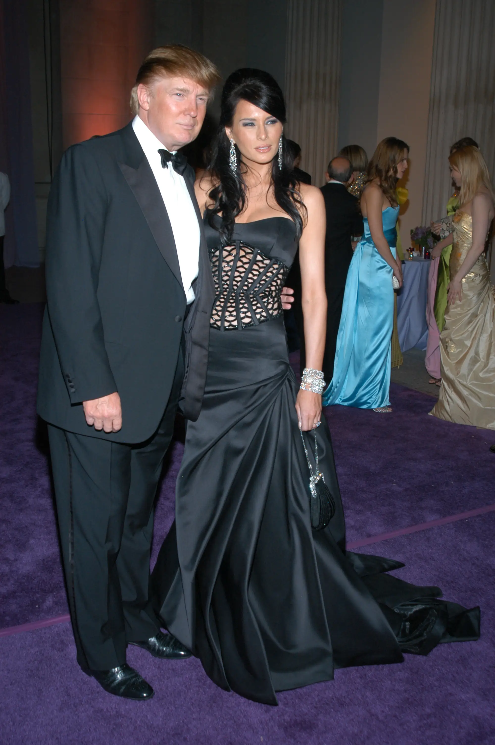 Donald Trump and Melania Trump pose on a purple carpet.