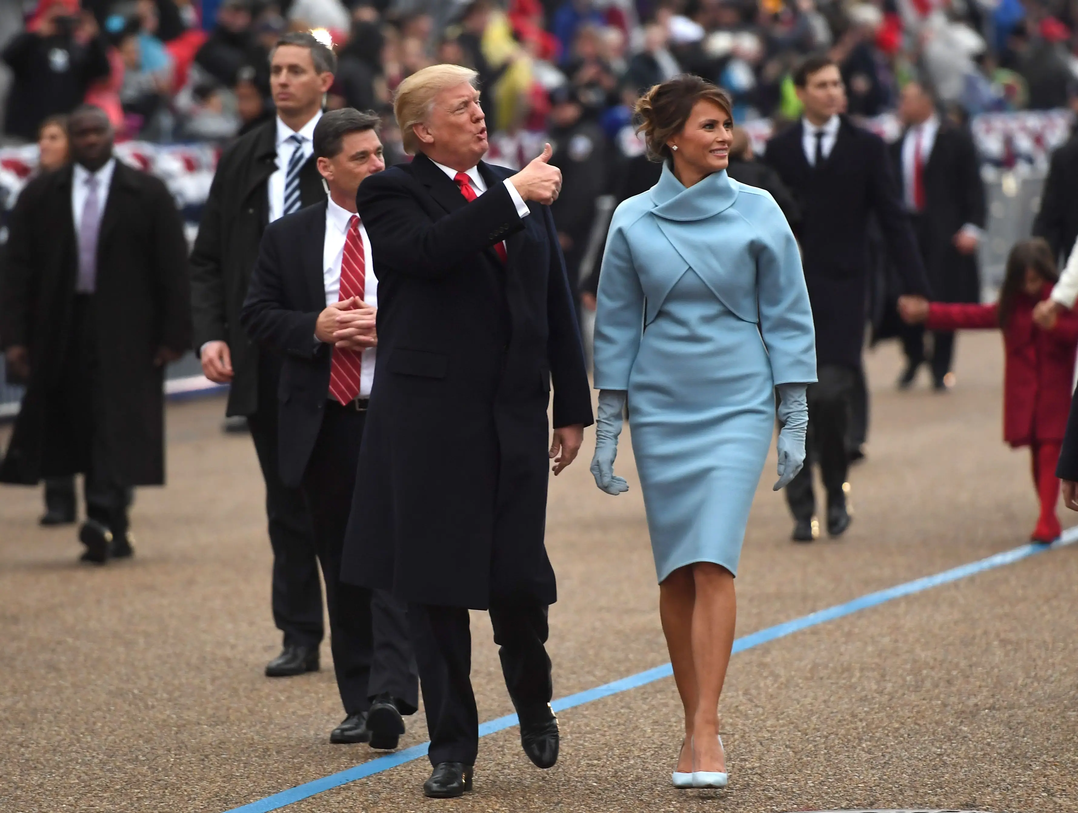 Donald and Melania Trump smile at crowds as they walk down the street.
