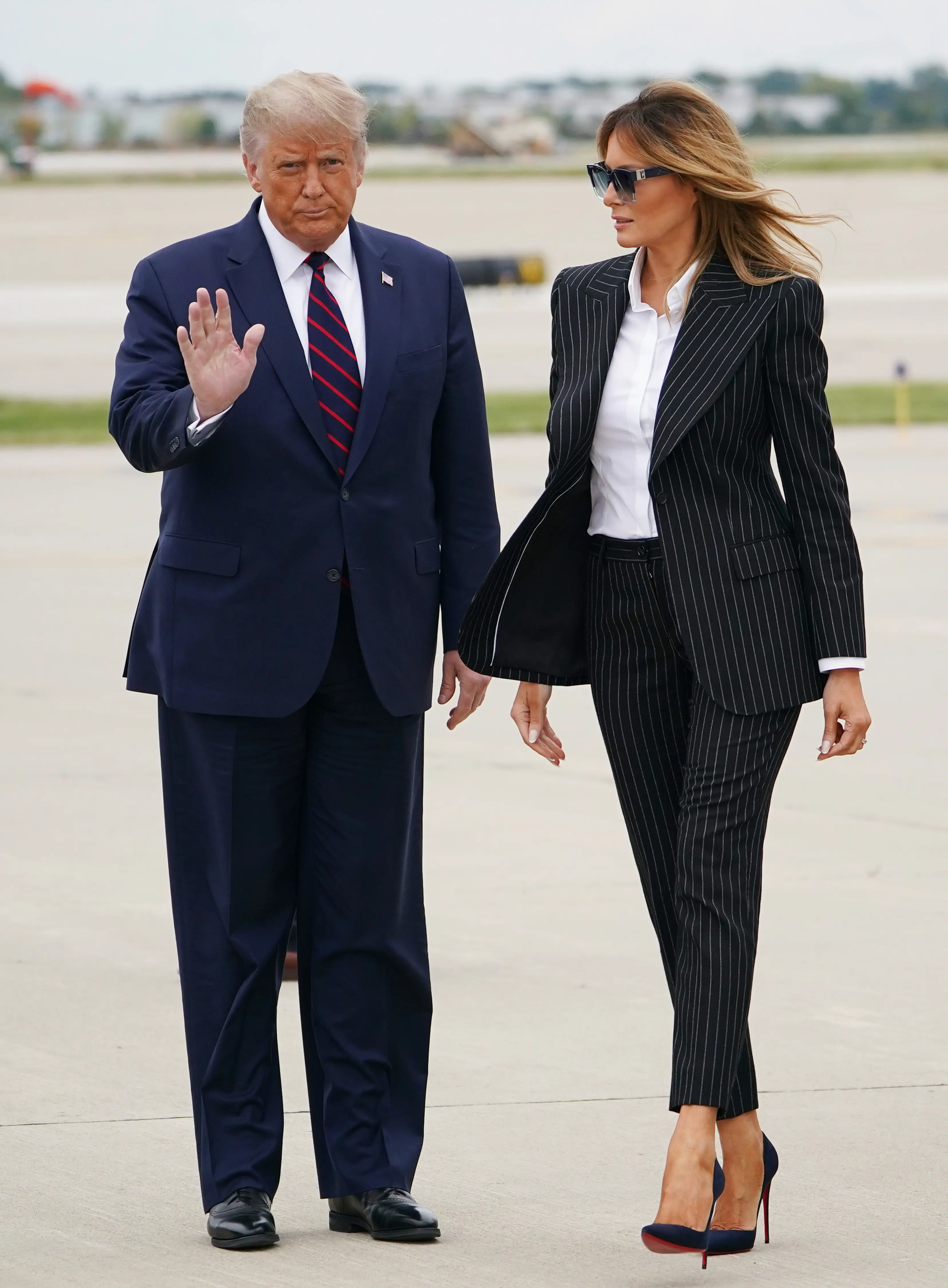 Donald and Melania Trump stand on a tarmac in suits.