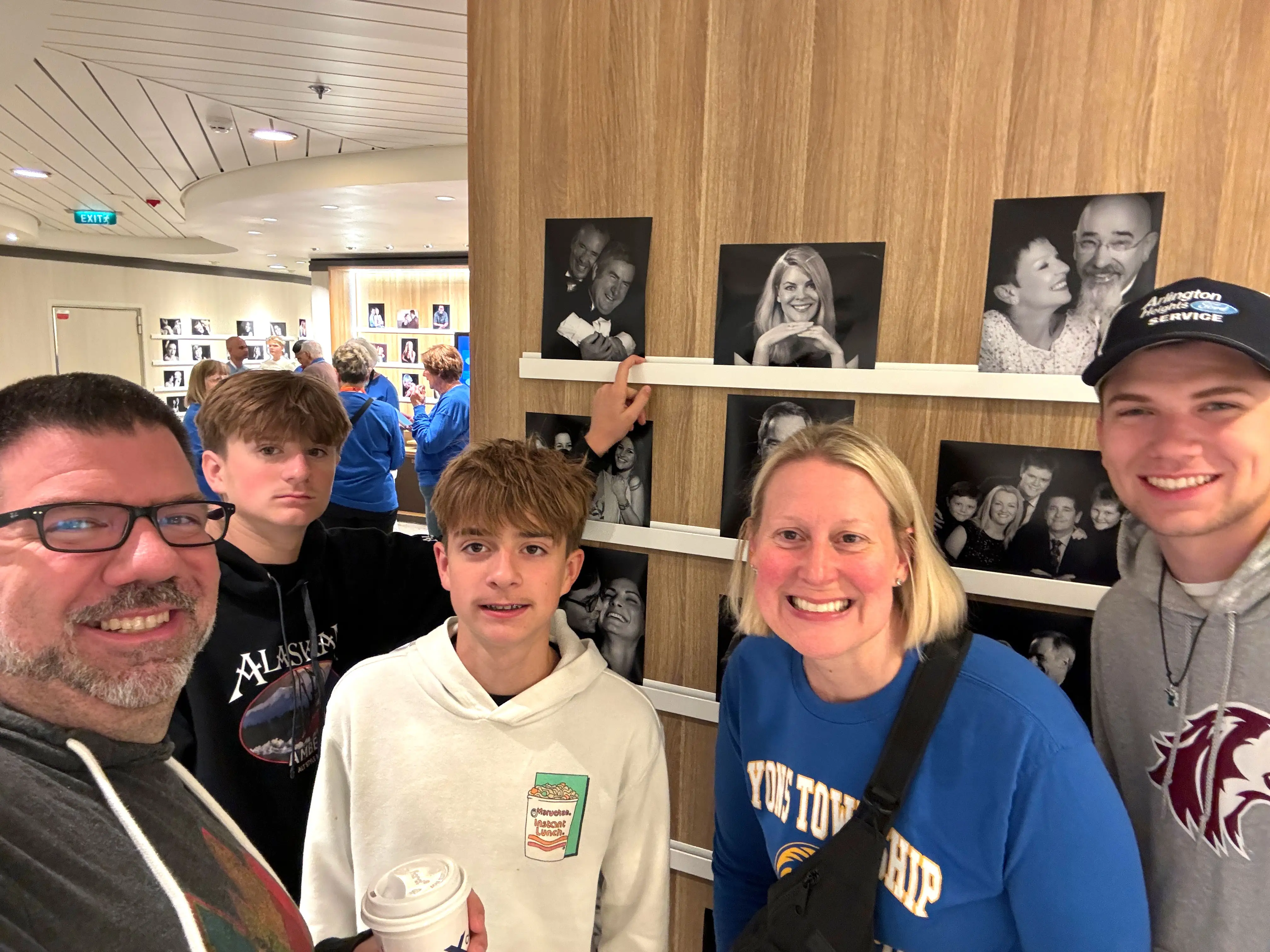 Chris, his wife, and three sons pose in sweatshirts in front of formal photographs.