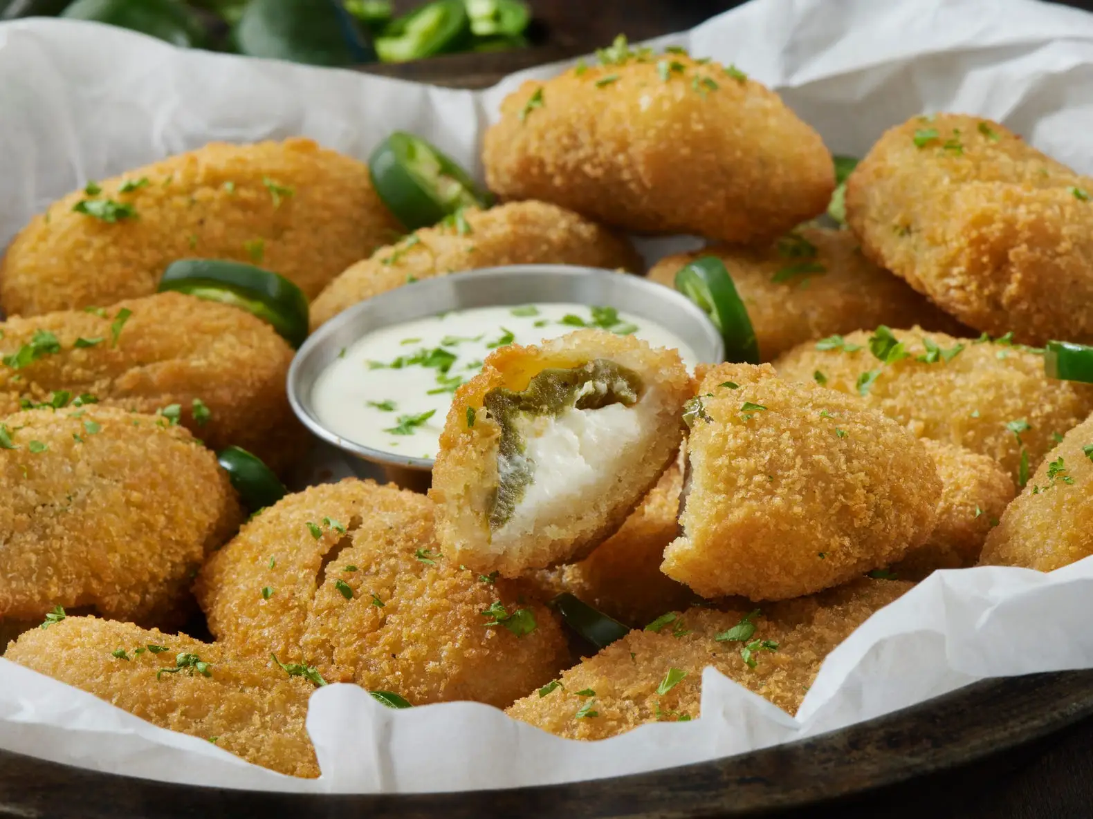 A tray with a white napkin filled with jalapeño poppers around a metal cup with a white dip in the center