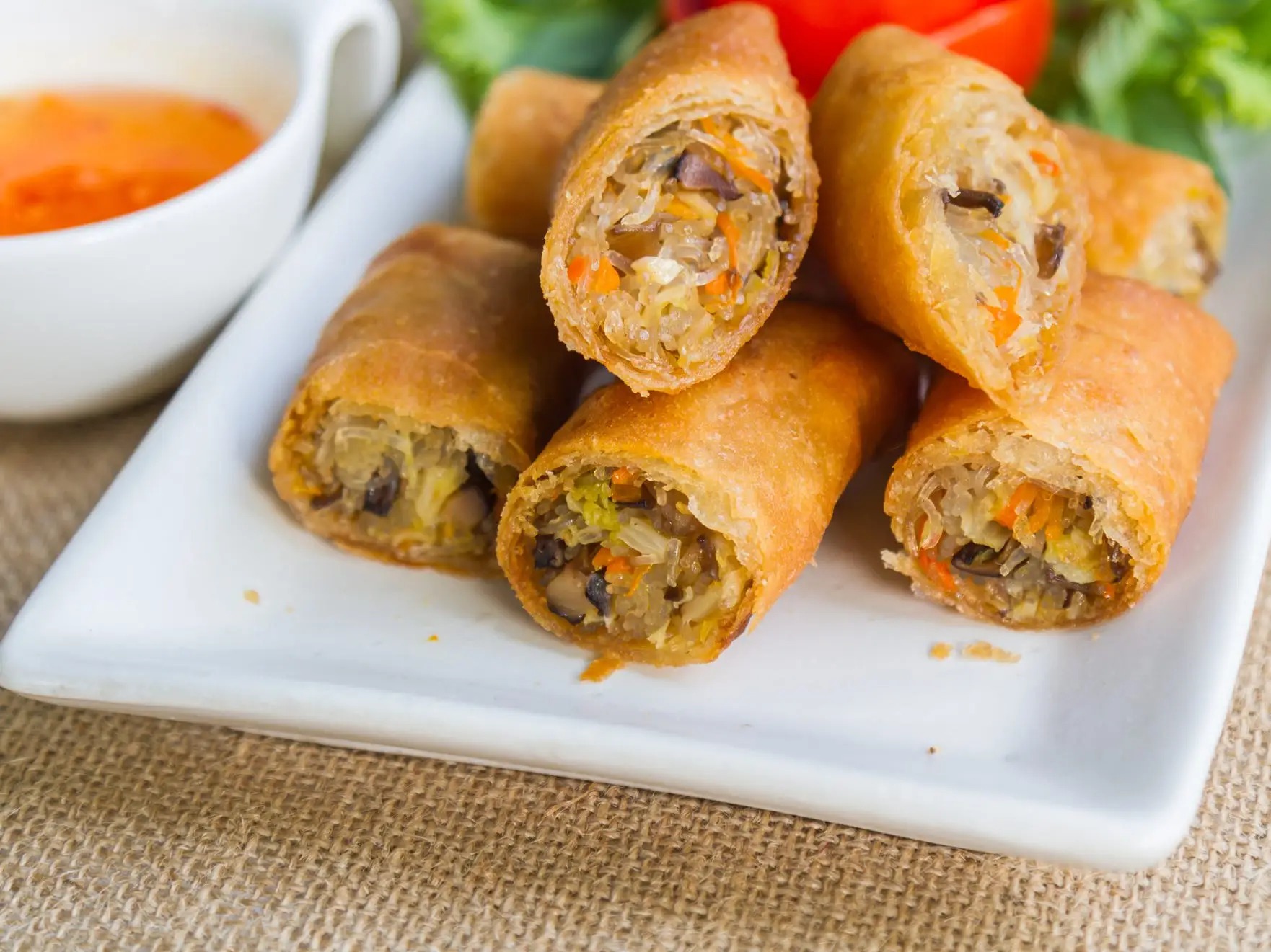 A white rectangular plate filled with golden brown vegetable spring rolls cut in half