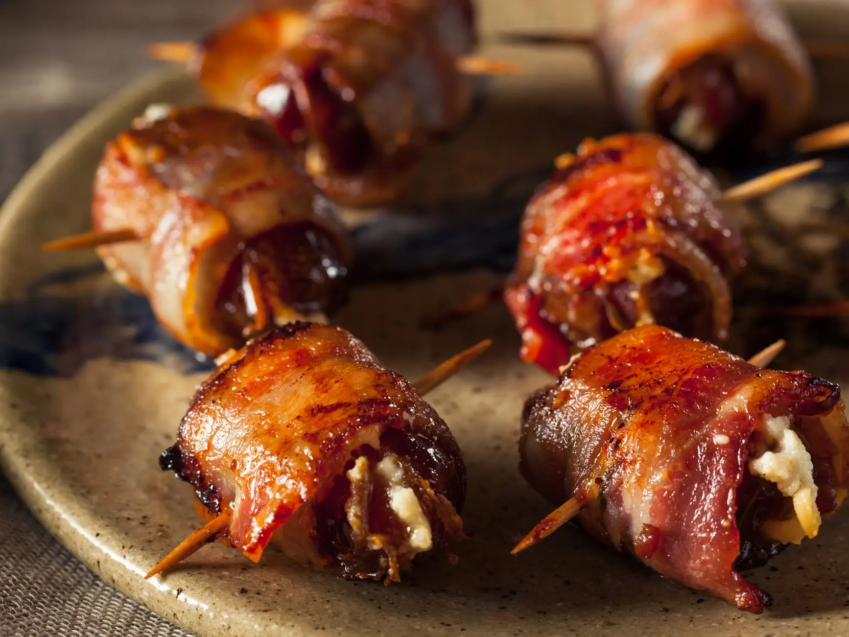 A gray ceramic plate filled with bacon wrapped dates speared with toothpicks
