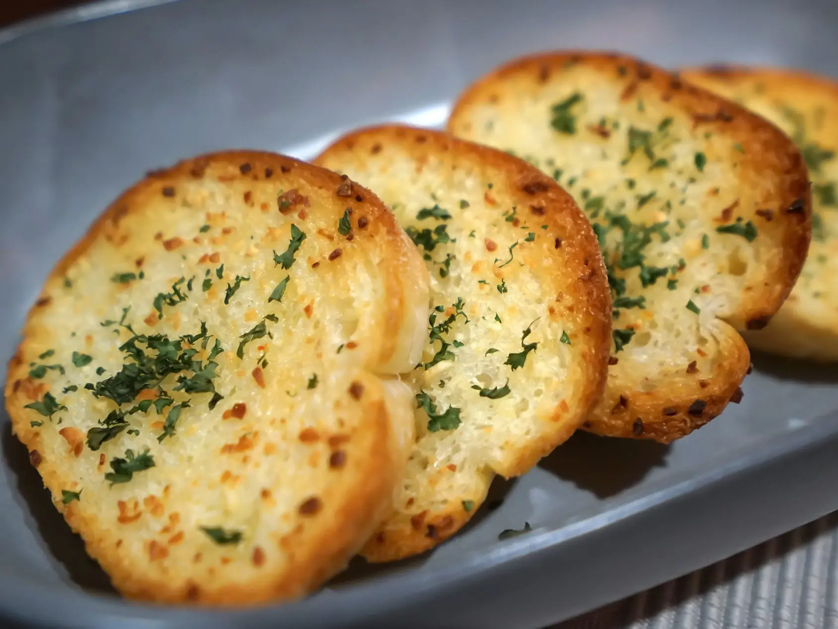 A gray serving dish with four small pieces of garlic bread with herbs on top