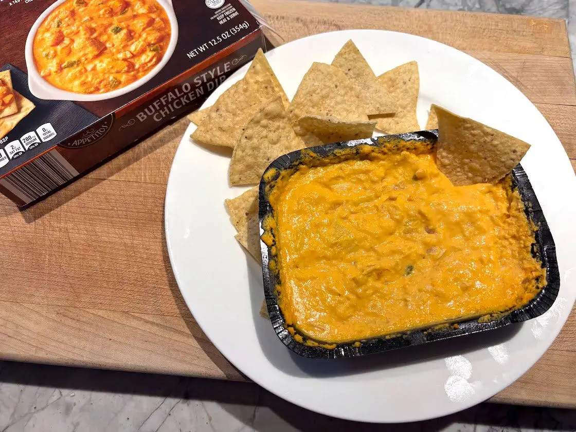 Buffalo-chicken dip with chips on a plate next to the box the product came in.
