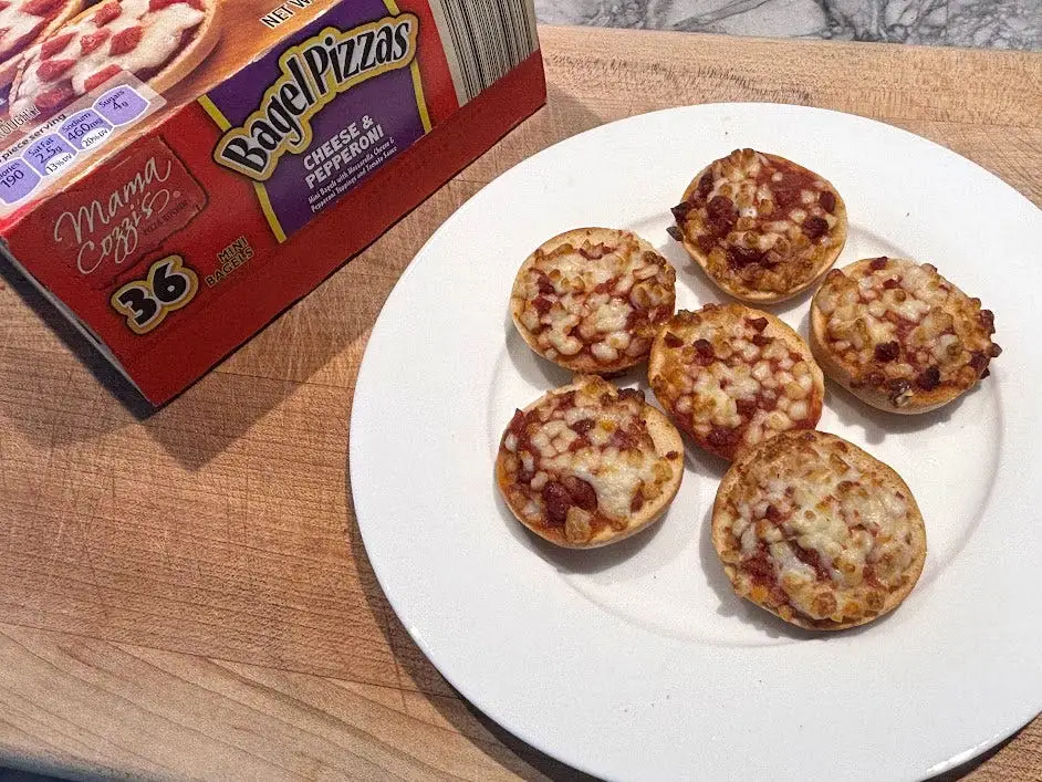Six pizza bagels on a white plate next to the box the product came in.