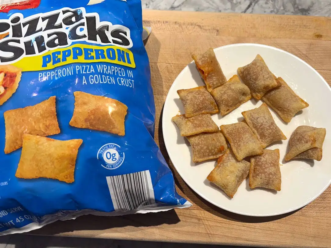 A plate of pizza rolls next to the box the product came in.