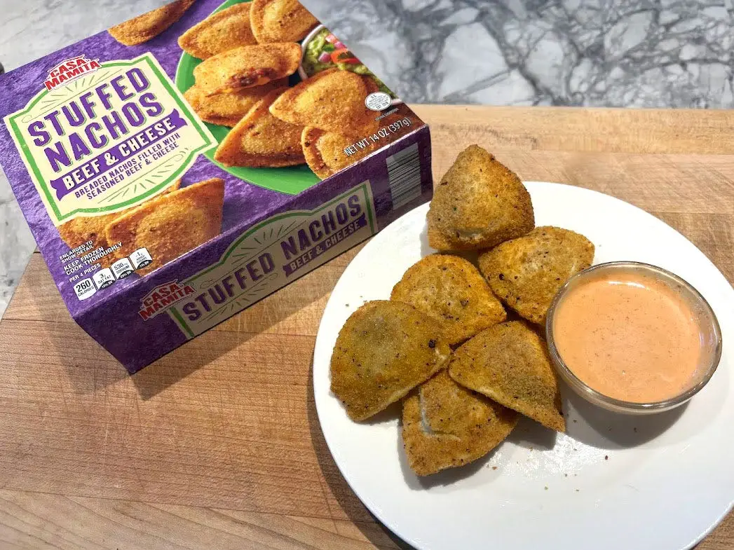 A box of Casa Mamita stuffed nachos next to a plate of the prepared product on a white plate with a small bowl of dipping sauce.