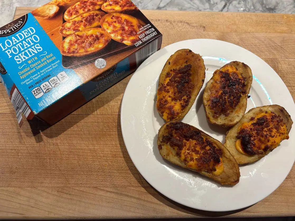 Four loaded baked potatoes on a white plate next to the packaging the product came in.