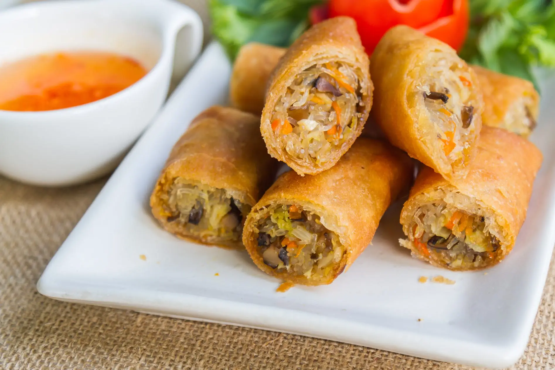 A white rectangular plate filled with golden brown vegetable spring rolls cut in half