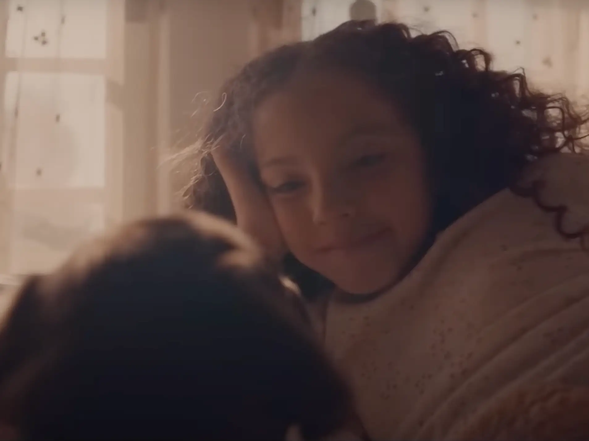 Little girl with curly hair laying on her bed smiling as she looks at her puppy.
