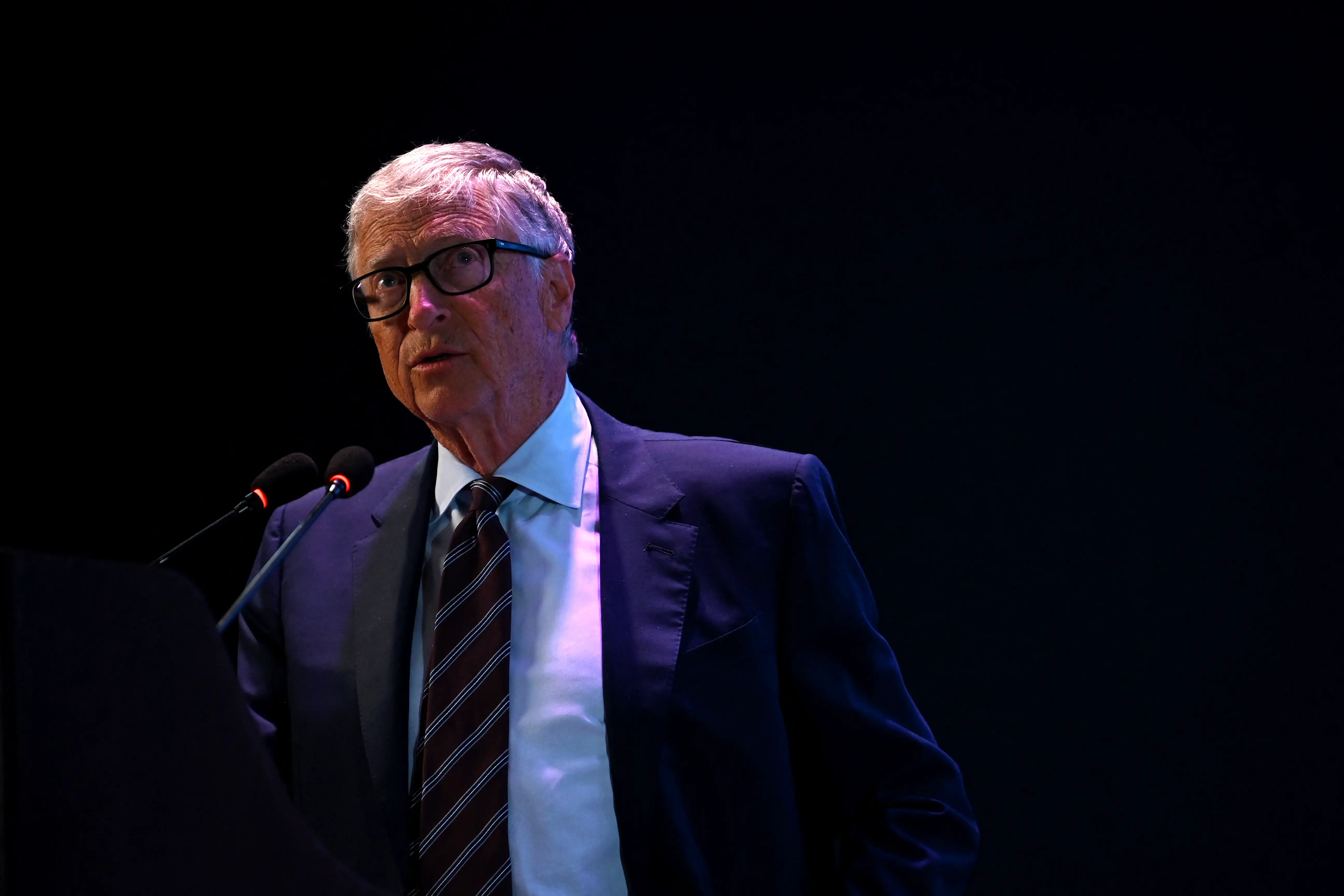Bill Gates in a suit and tie speaking into two microphones.