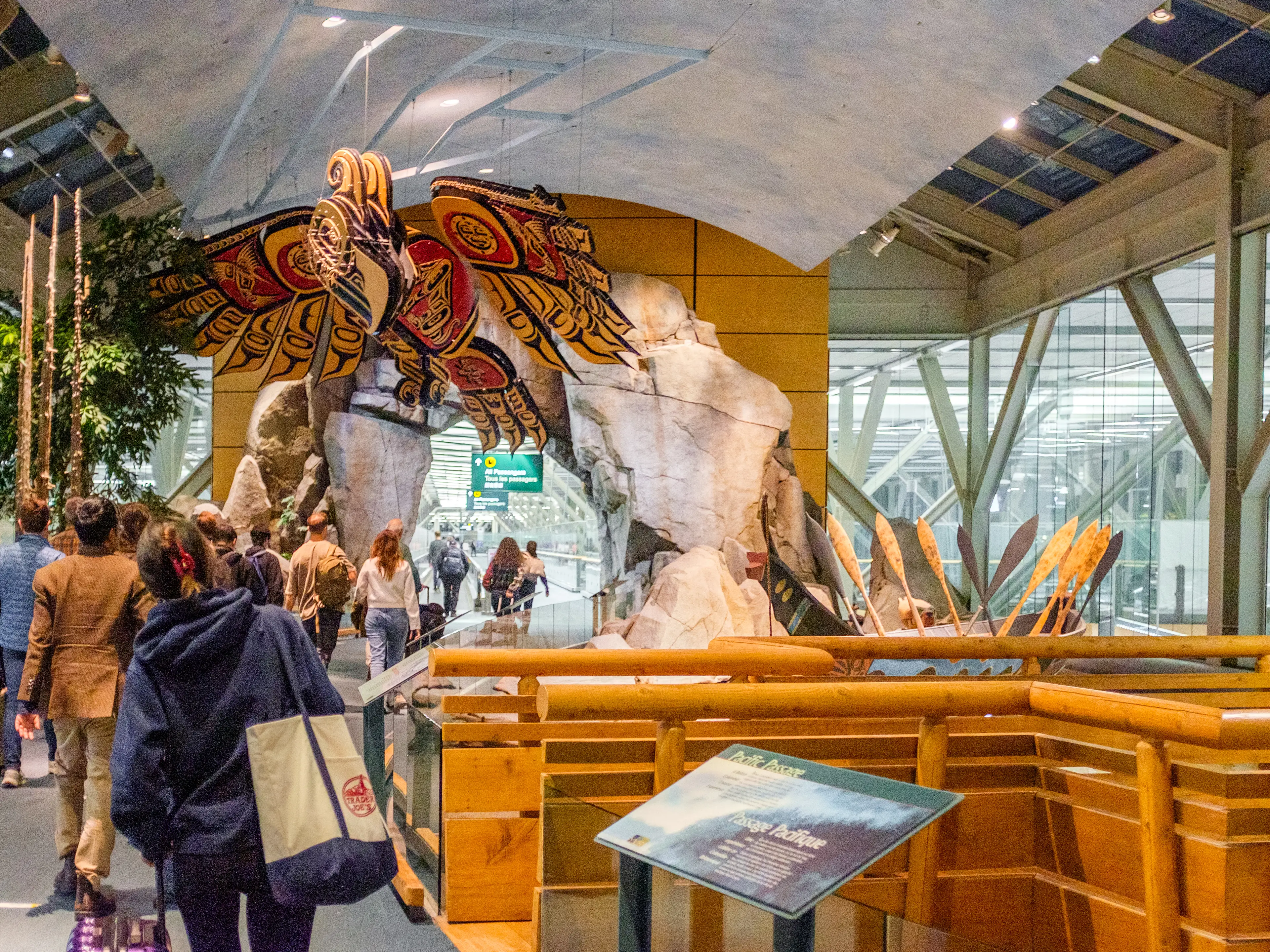 Travelers walk through an airport exhibit with a pond on the right and a bird sculpture above