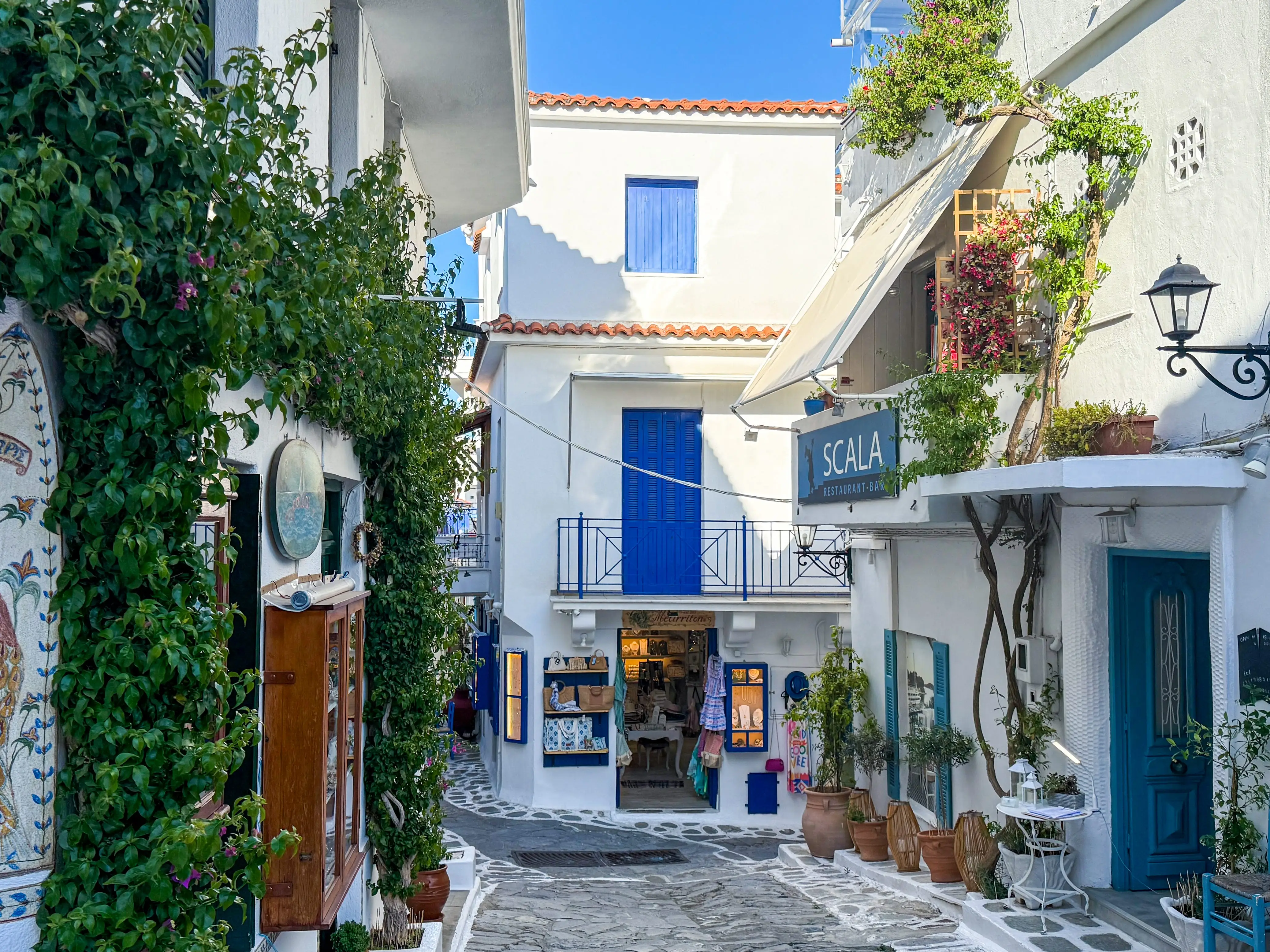 A view down a street in Skiathos, lined with whitewashed buildings, blue doors, windows, and balconies.