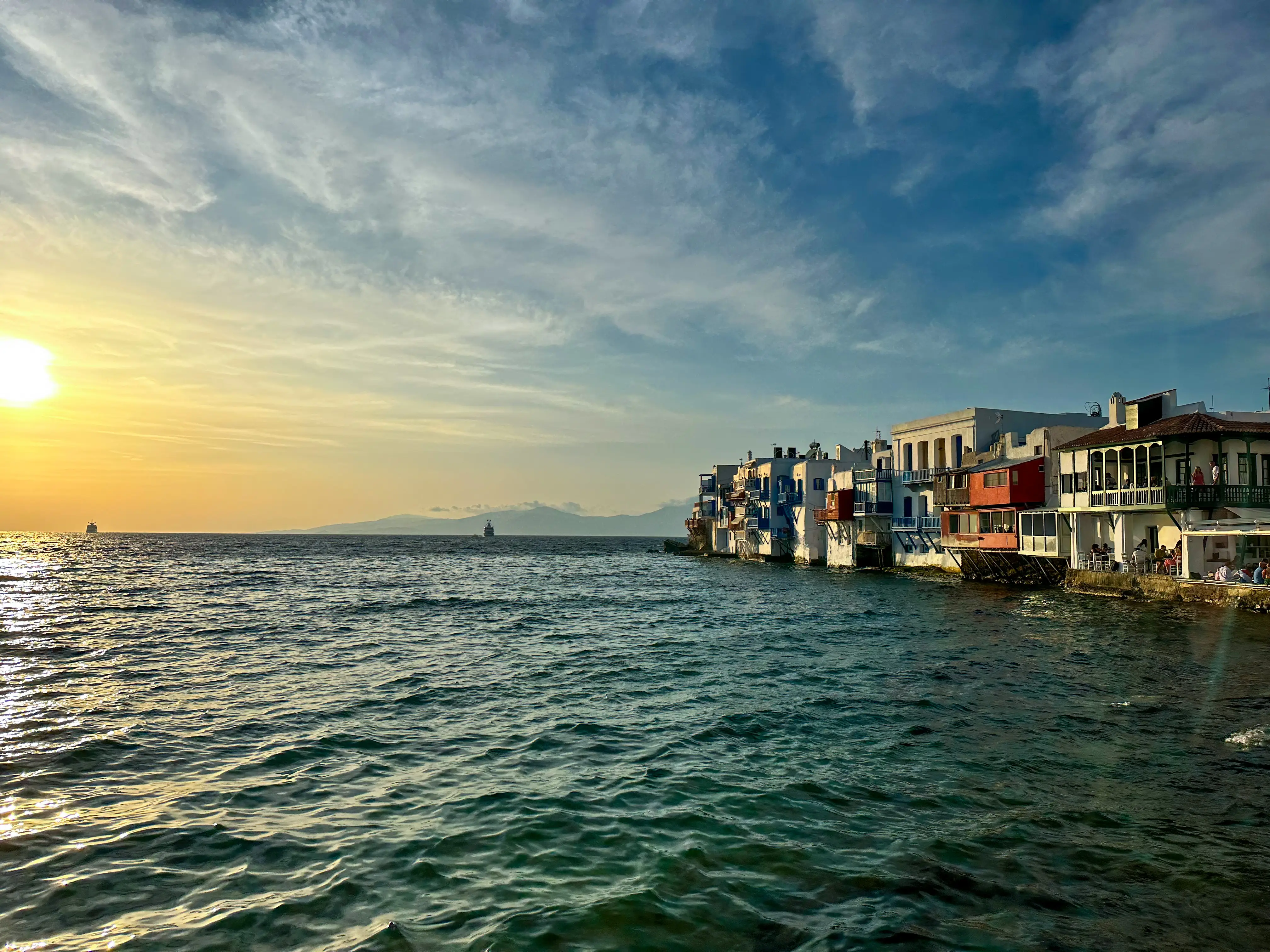 A view of the water during sunset in Mykonos, with colorful buildings lining the coast.