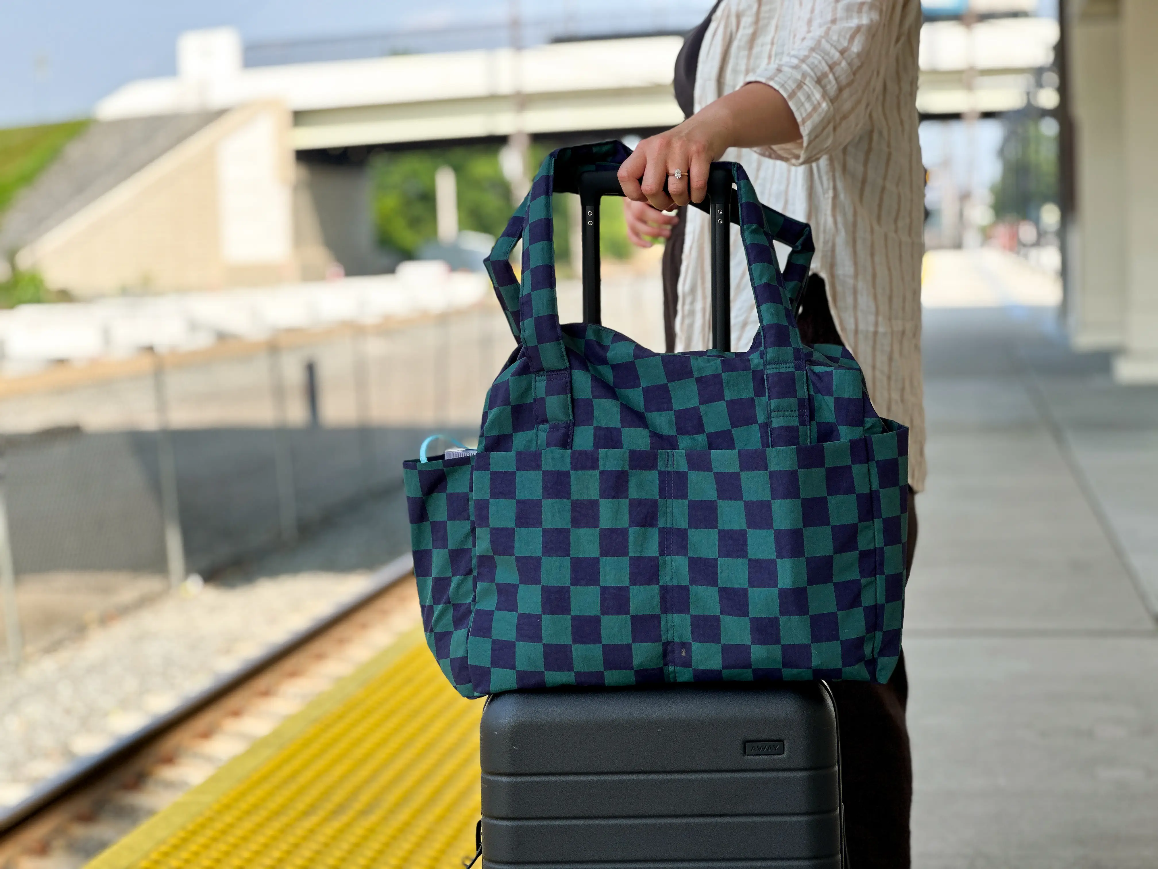 A blue checkered bag with pockets on top of a black suitcase.