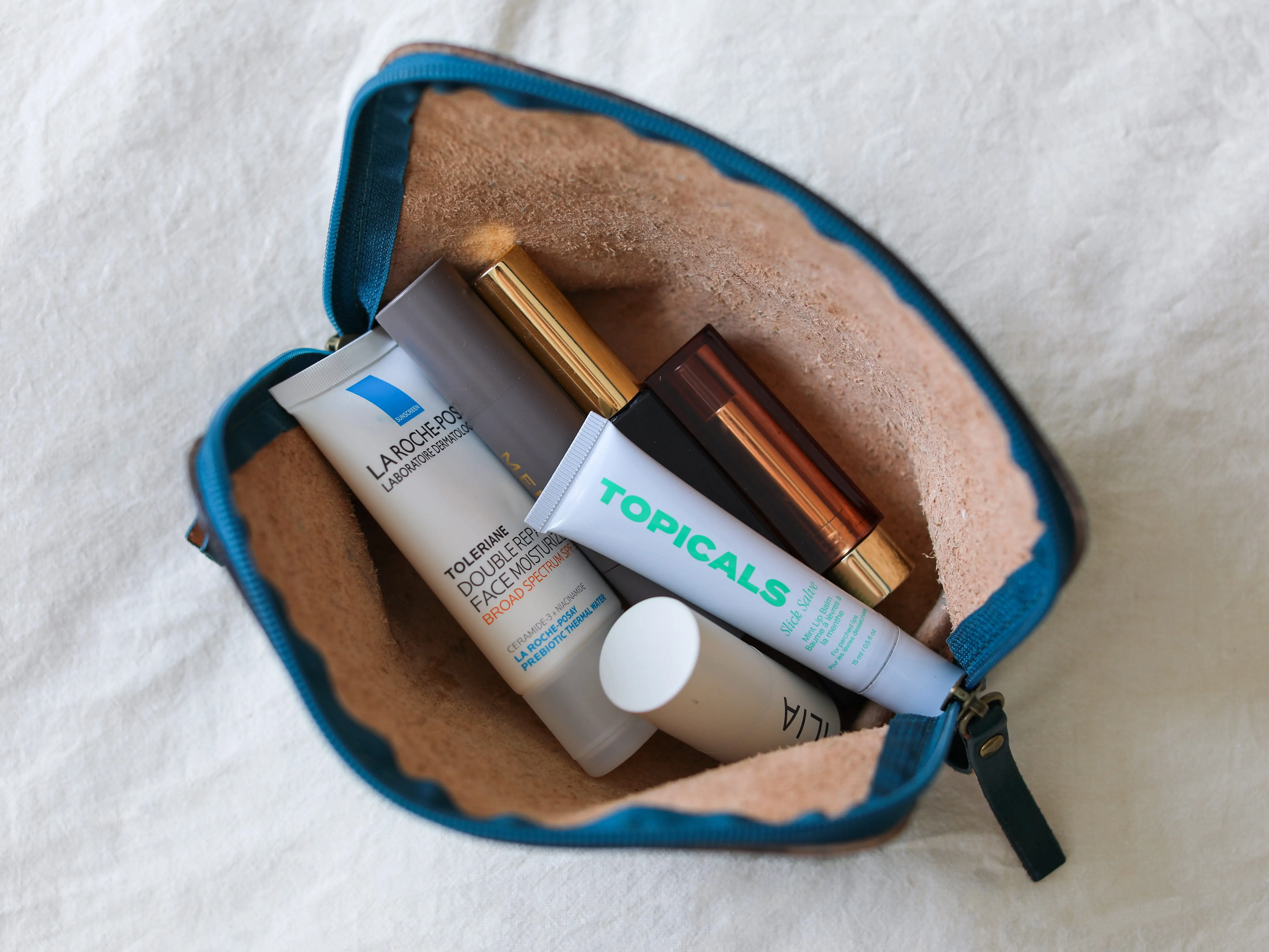 An unzipped makeup bag filled with skincare and cosmetic products.