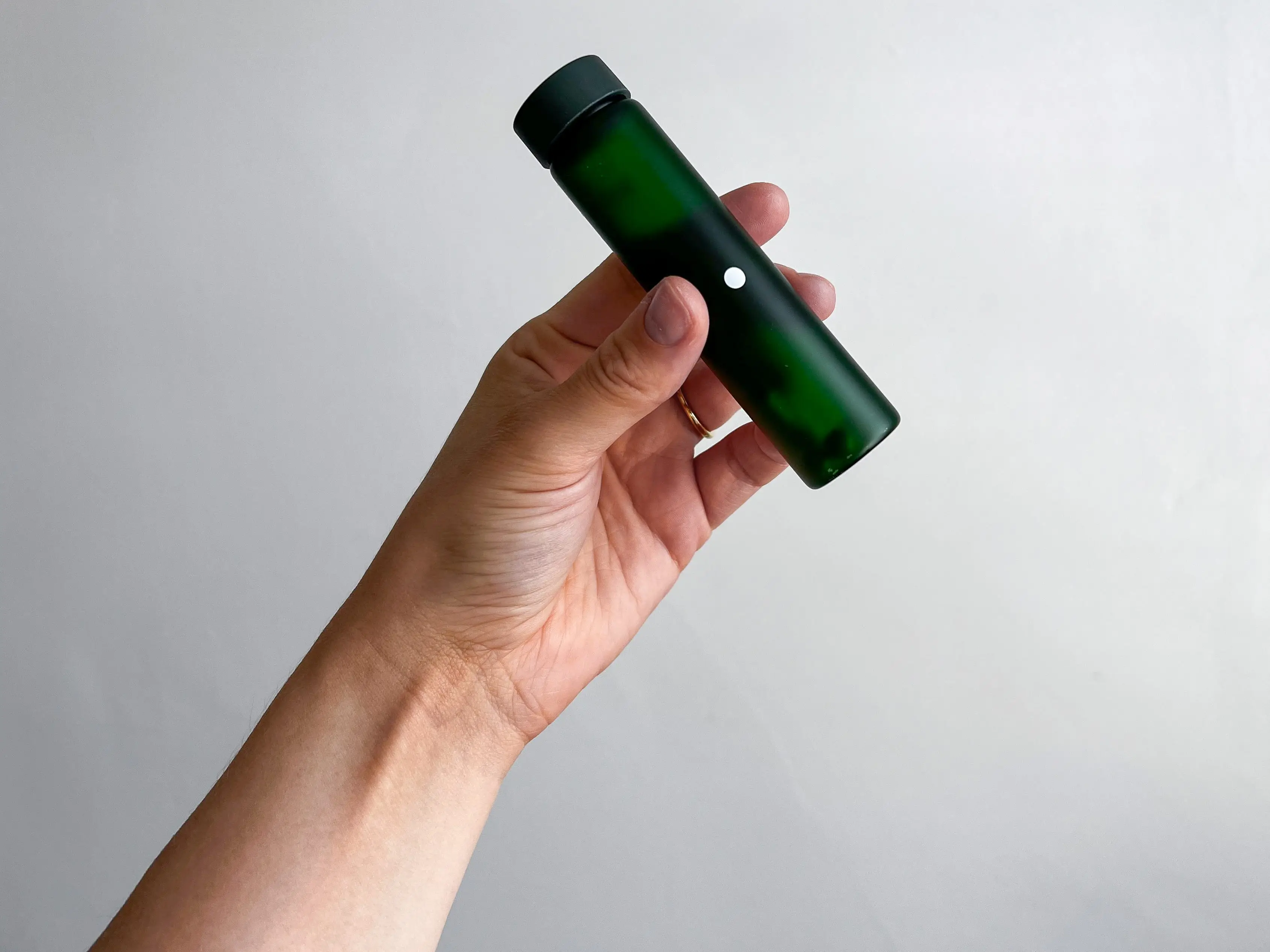 A hand holding a tall green pill case.
