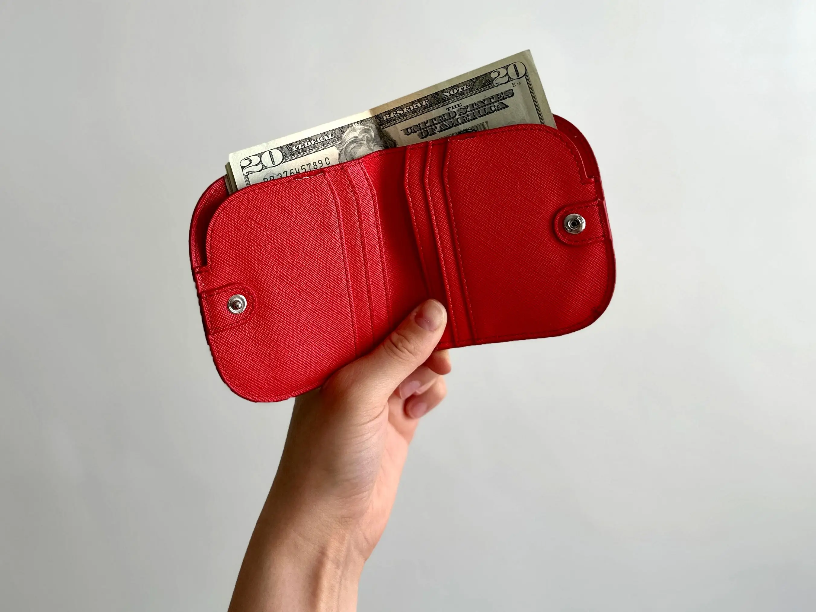 A hand holding a red wallet with a $20 bill sticking out of the top.