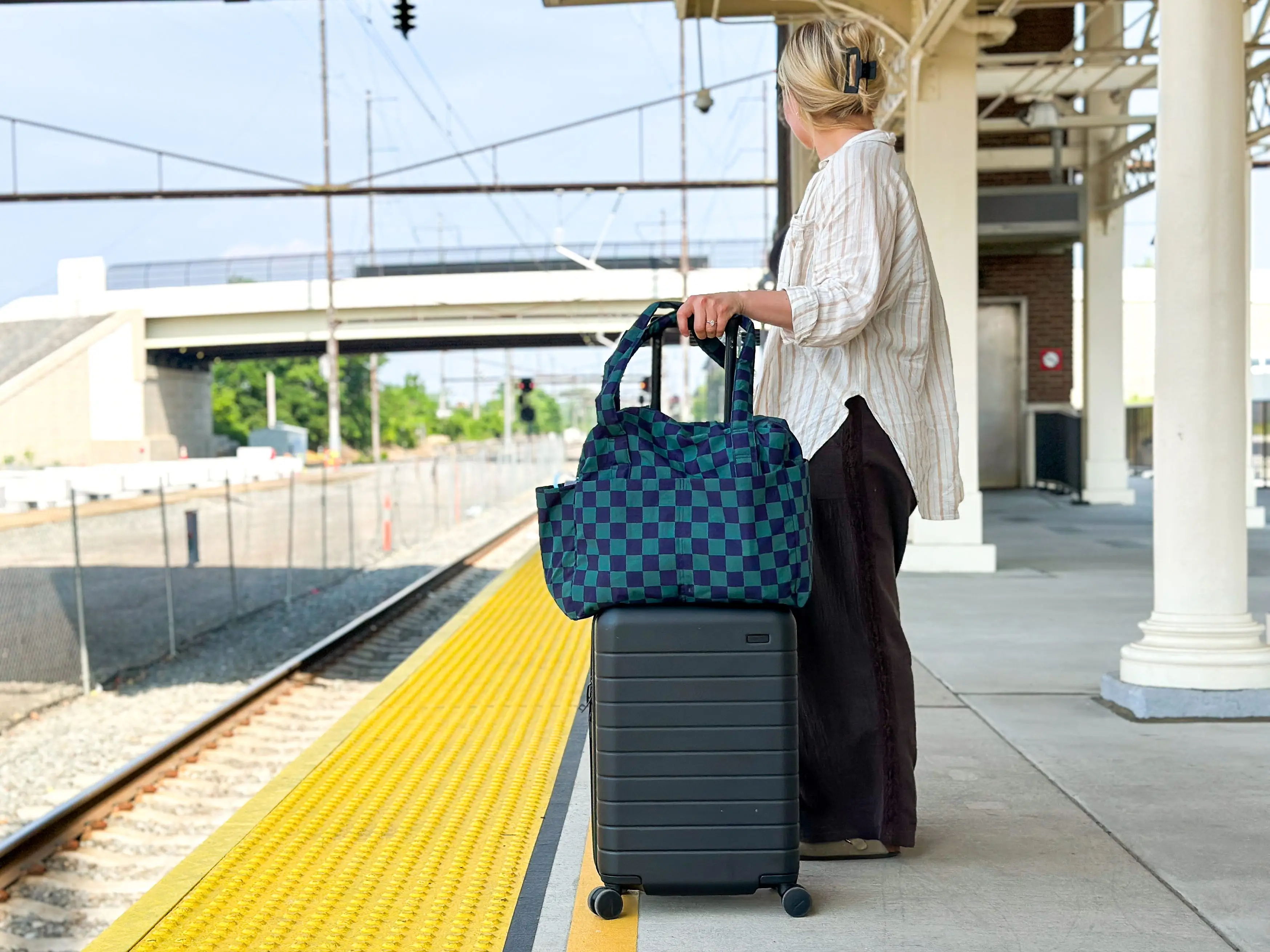 Kylie holds a bag on top of a suitcase on a train platform.