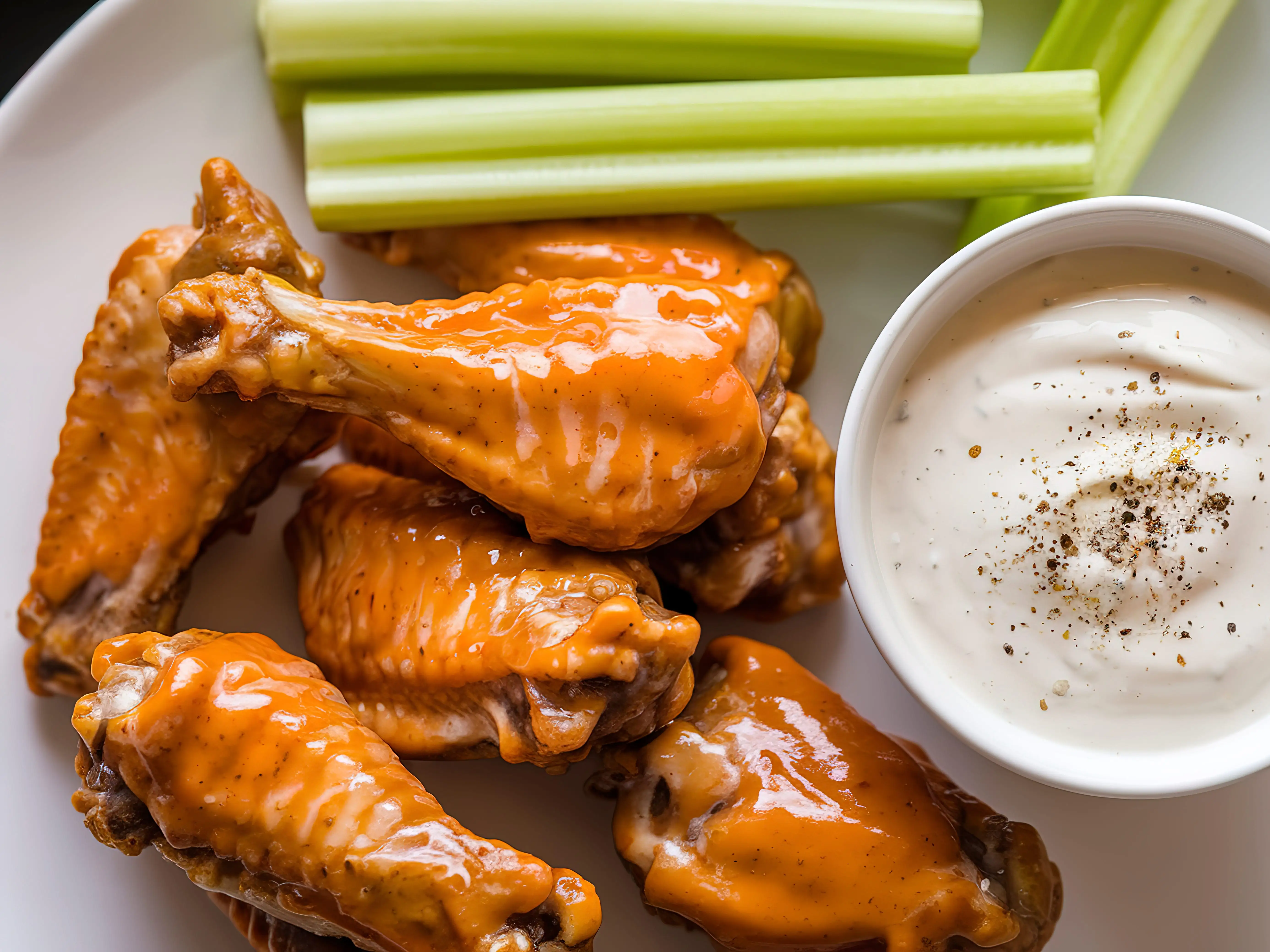 A plate of glazed chicken wings with a side of celery sticks