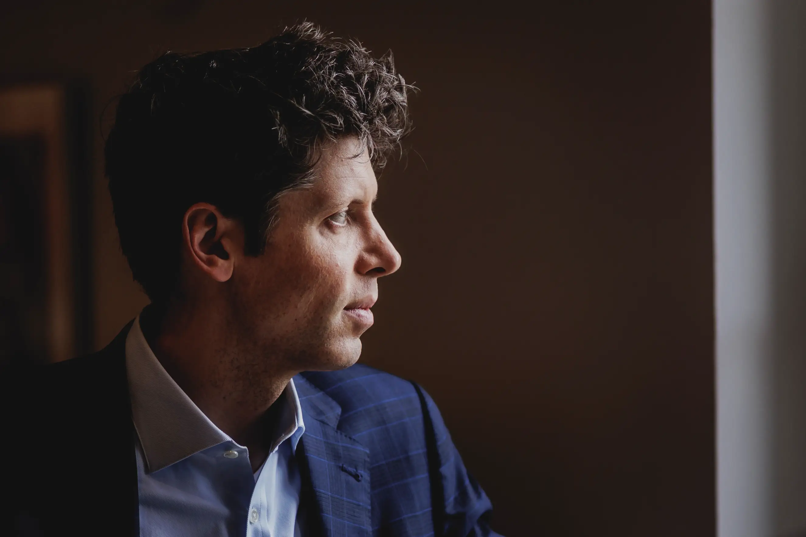 Sam Altman's profile, standing in front of a window.