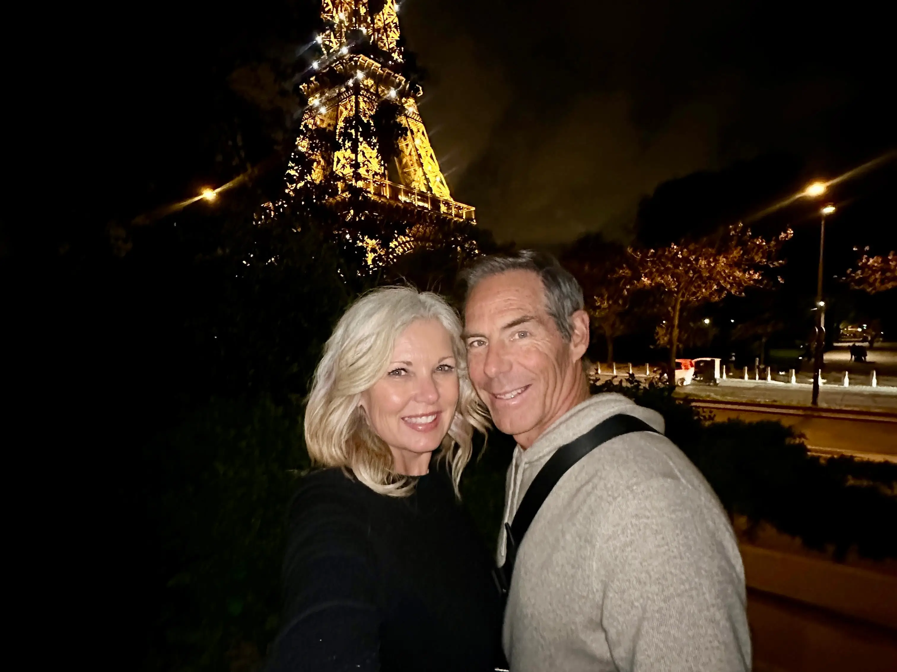The author and her husband posing in Paris at night with the Eiffel Tower sparkling in the background.