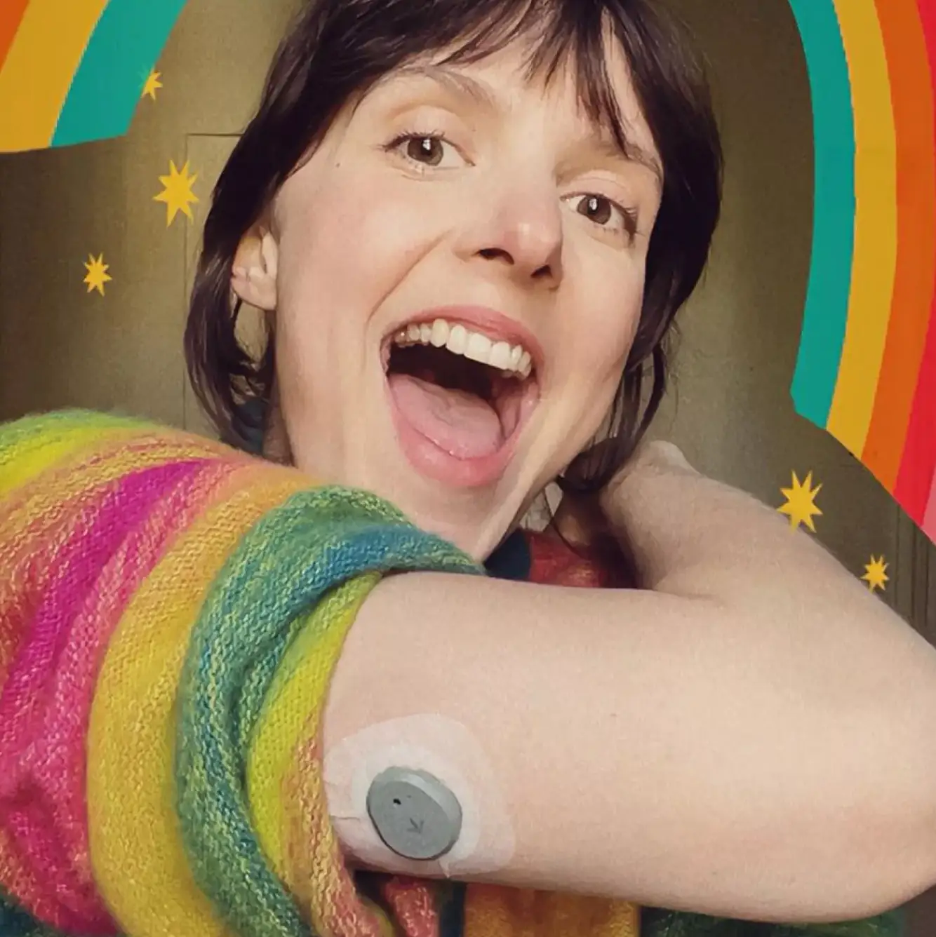 a woman smiling in a brightly colored outfit and wearing a continuous glucose monitor or CGM on the back of her upper arm.