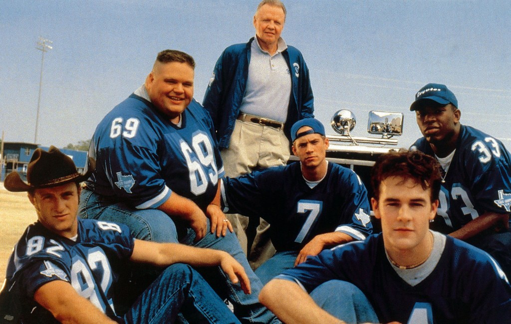 Six actors from Varsity Blues, Scott Caan, Ron Lester, Jon Voight, Paul Walker, James Van Der Beek, and Eliel Swinton, pose in their football uniforms and a coach's jacket.