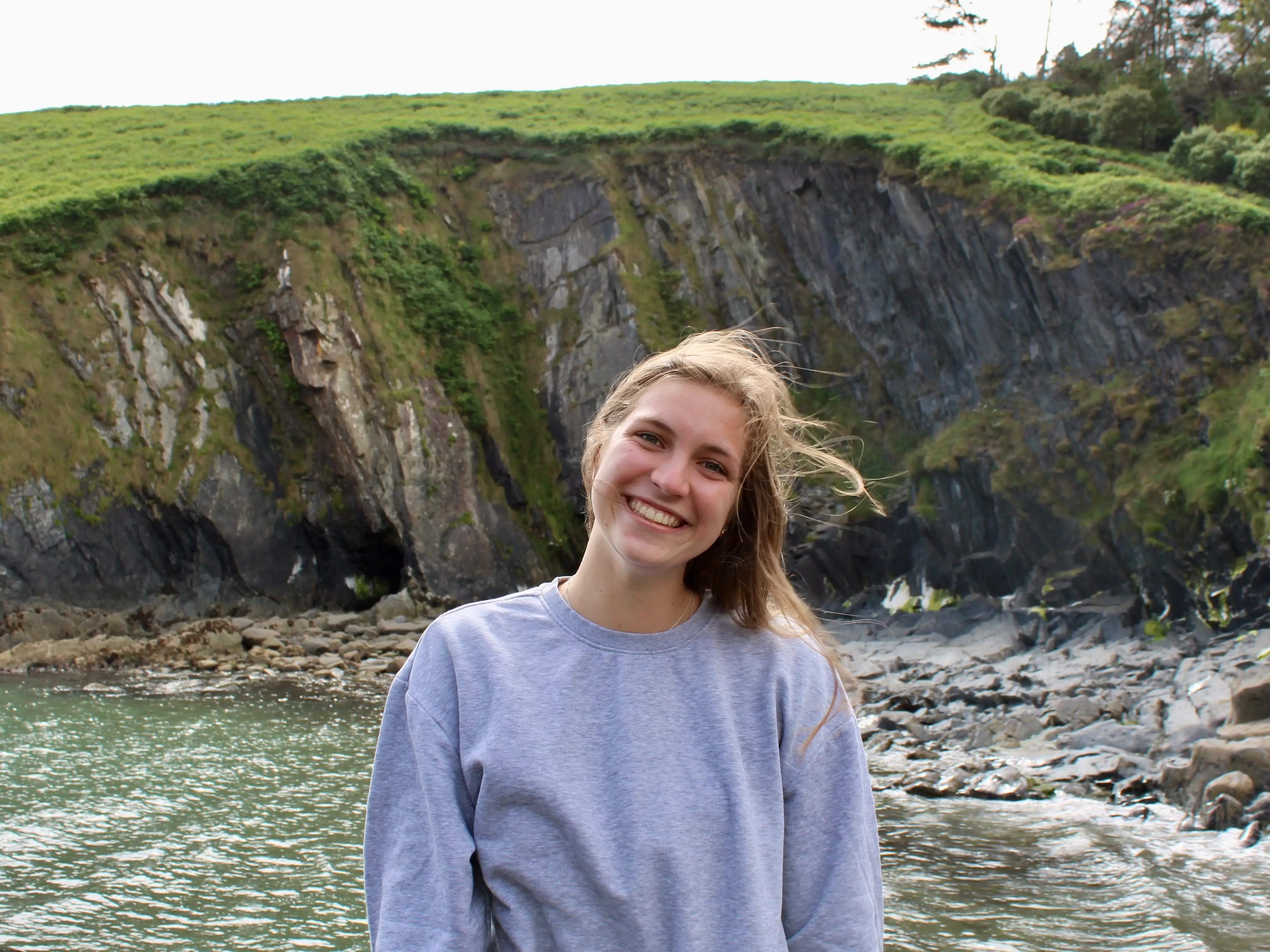 Hannah stands in front of a cliff in Ireland.