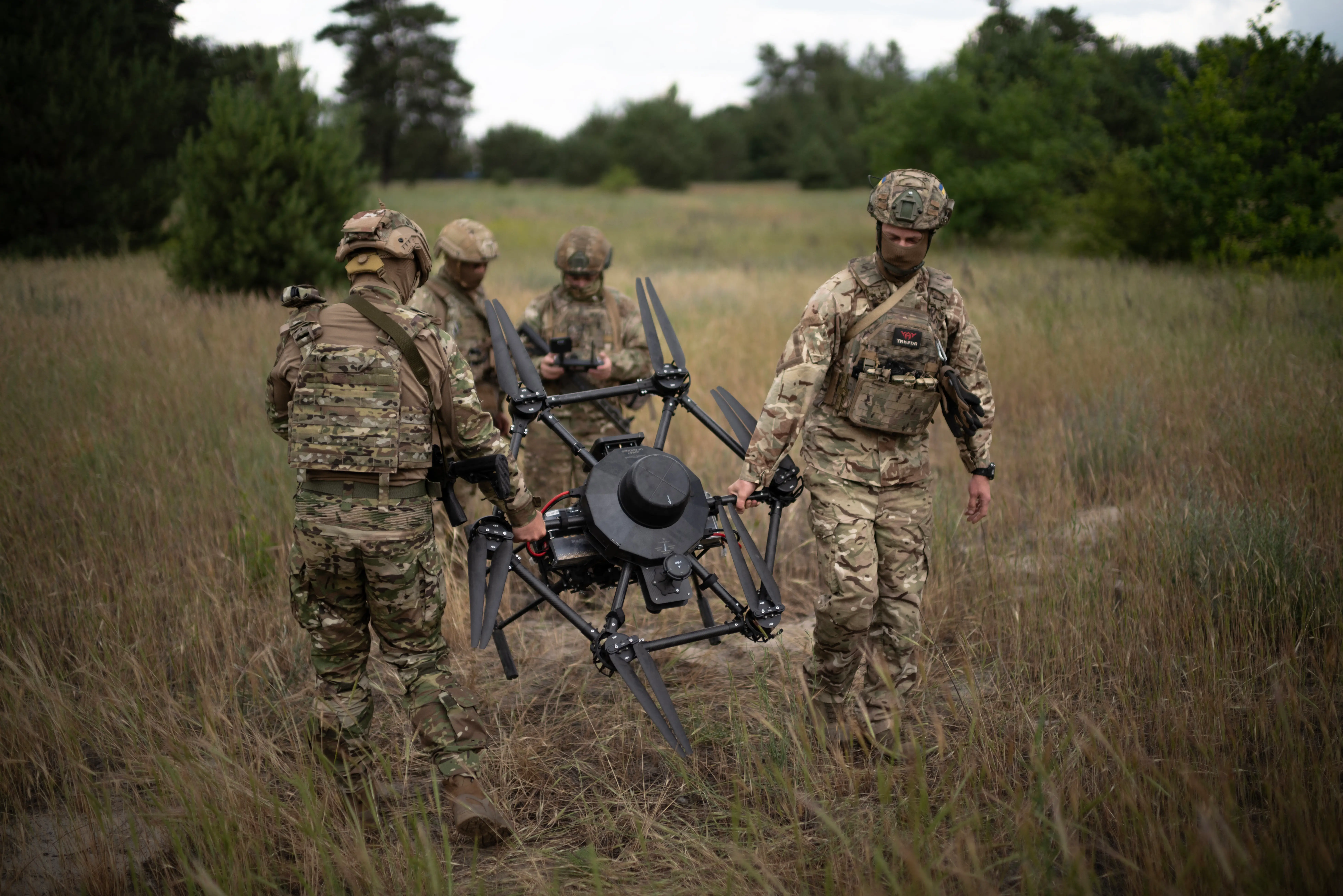 Four figures in camouflage around a large black drone in a field