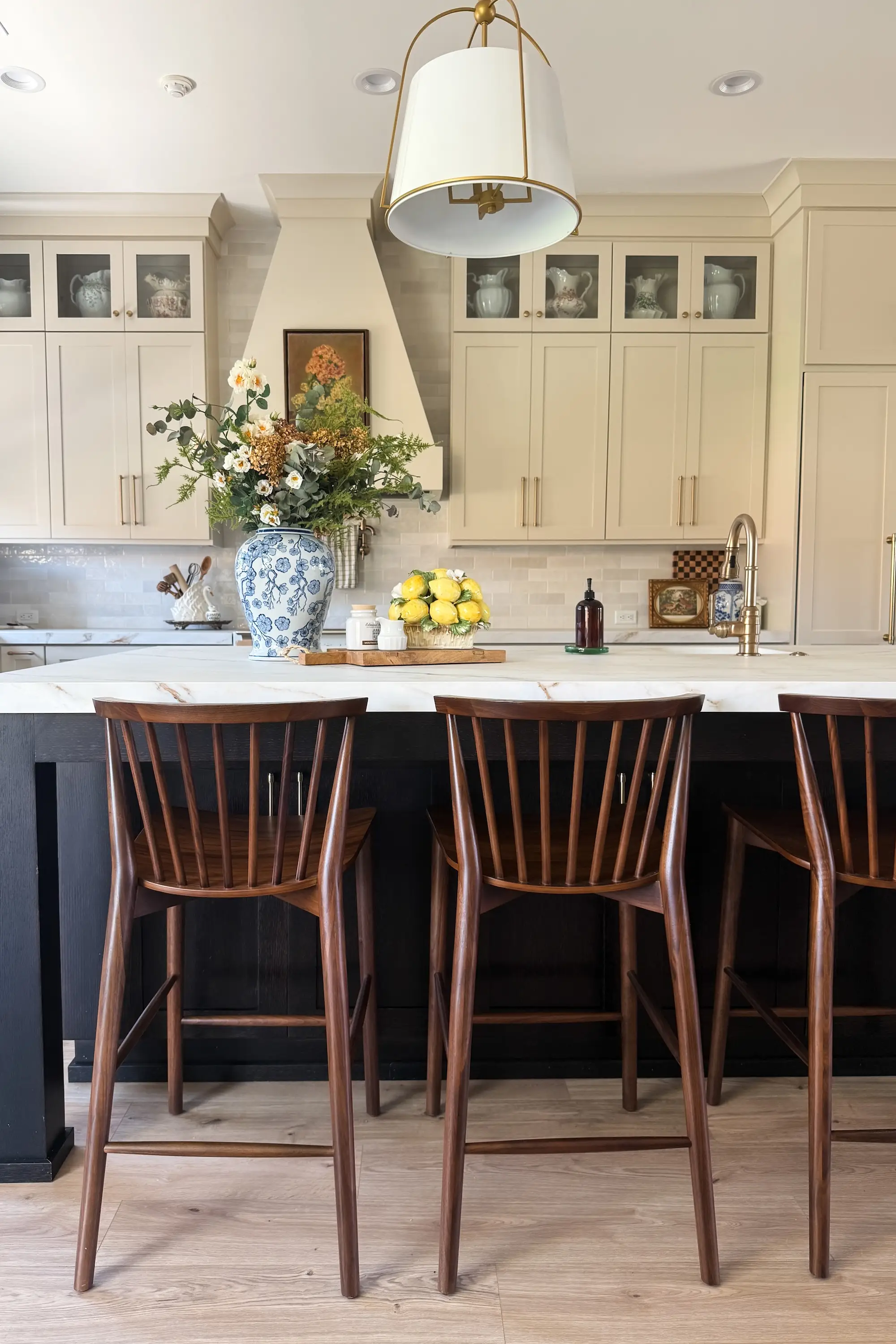 A kitchen with a black island with white countertops and cream cabinetry. Wooden chairs sit against the island.
