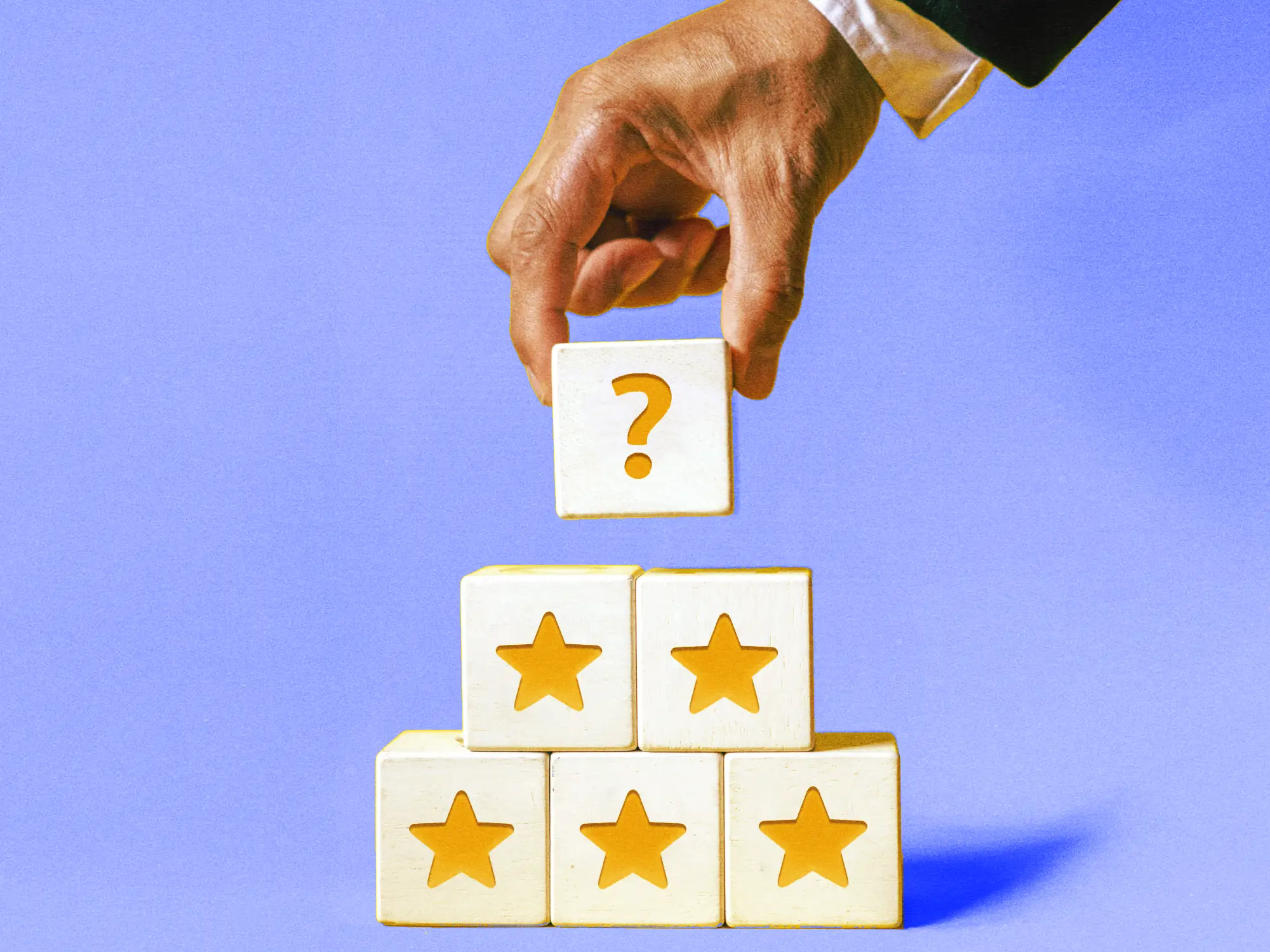 A hand holding a wooden block with a question mark, above a pyramid of gold stars.