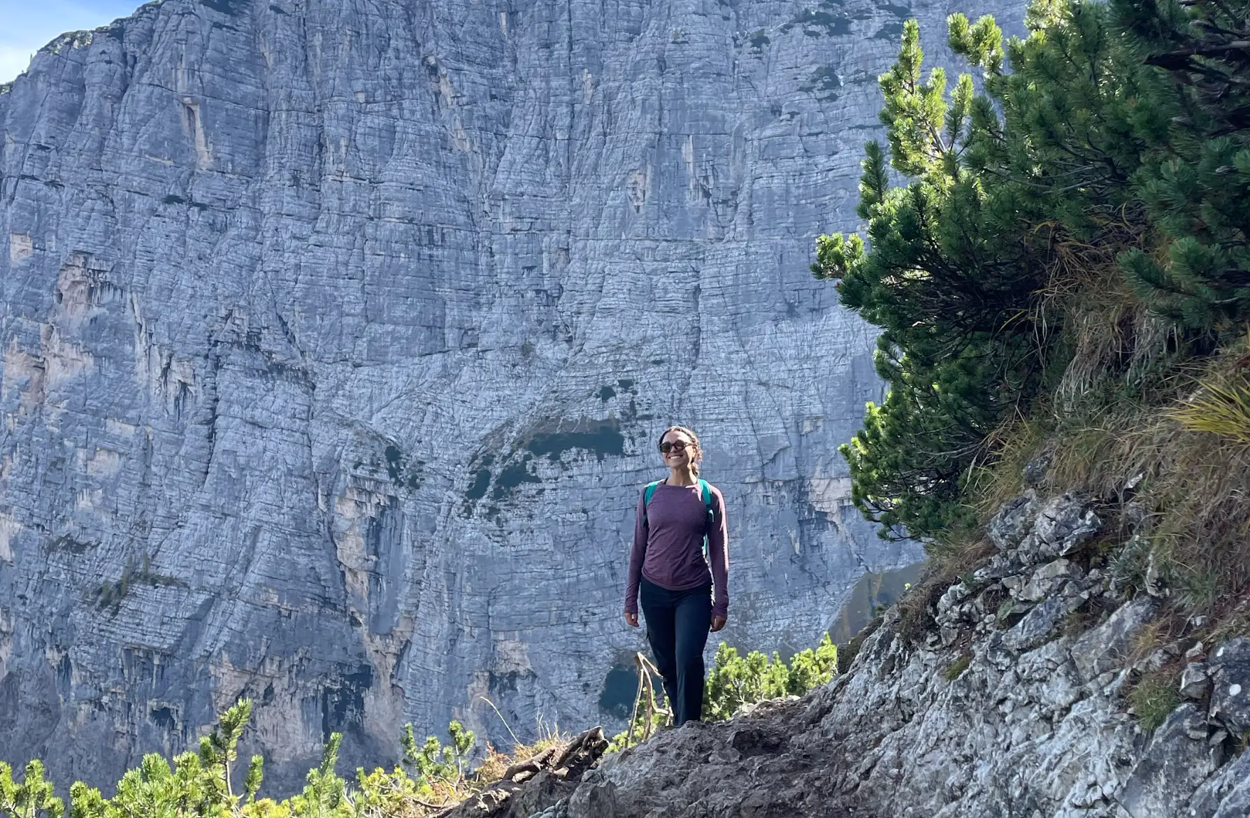 The writer standing with a backpack at Lago Sorapis in Italy, with a mountain in the background.