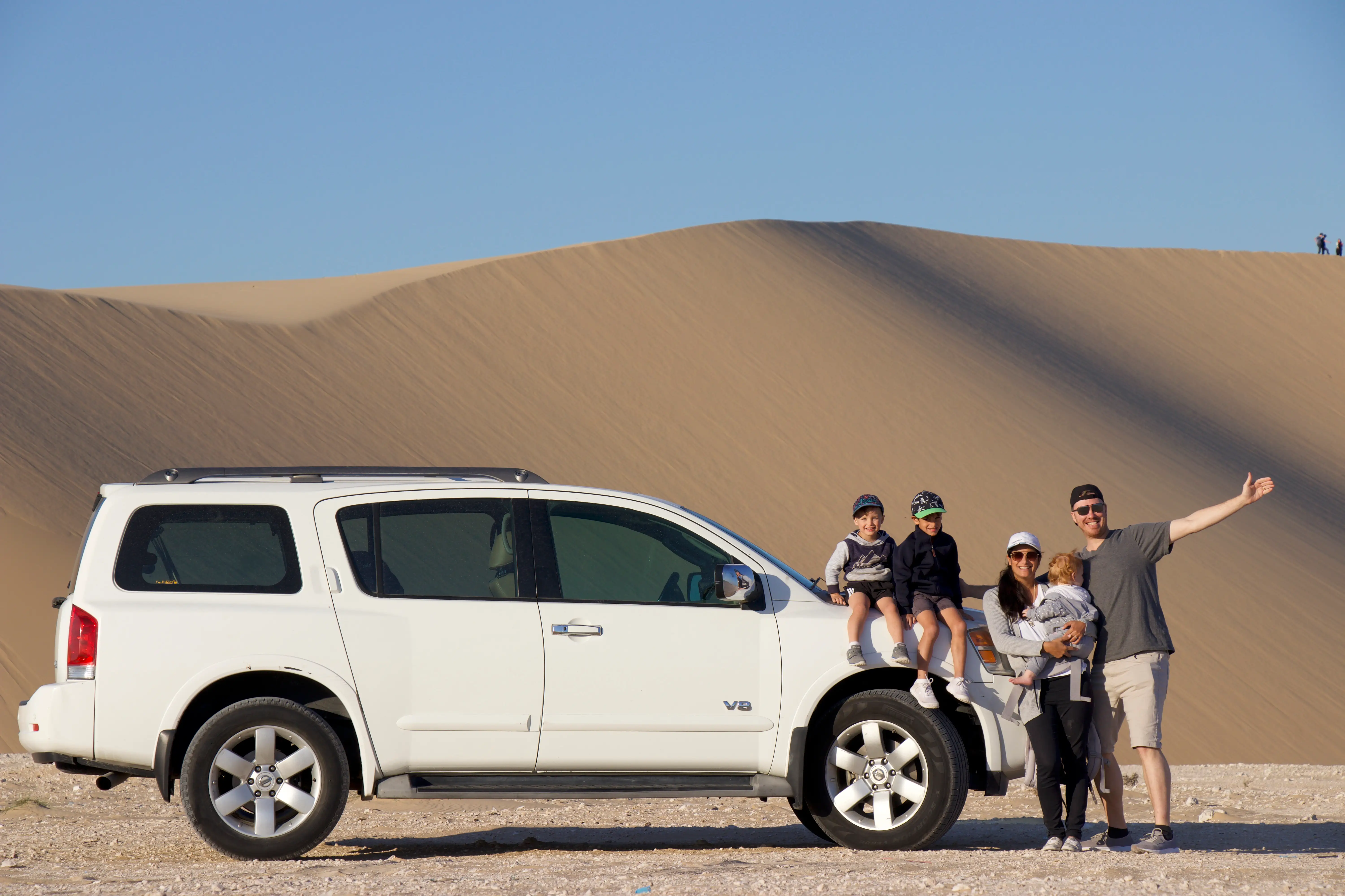 A family posing with their car in the sand dunes of Qatar.
