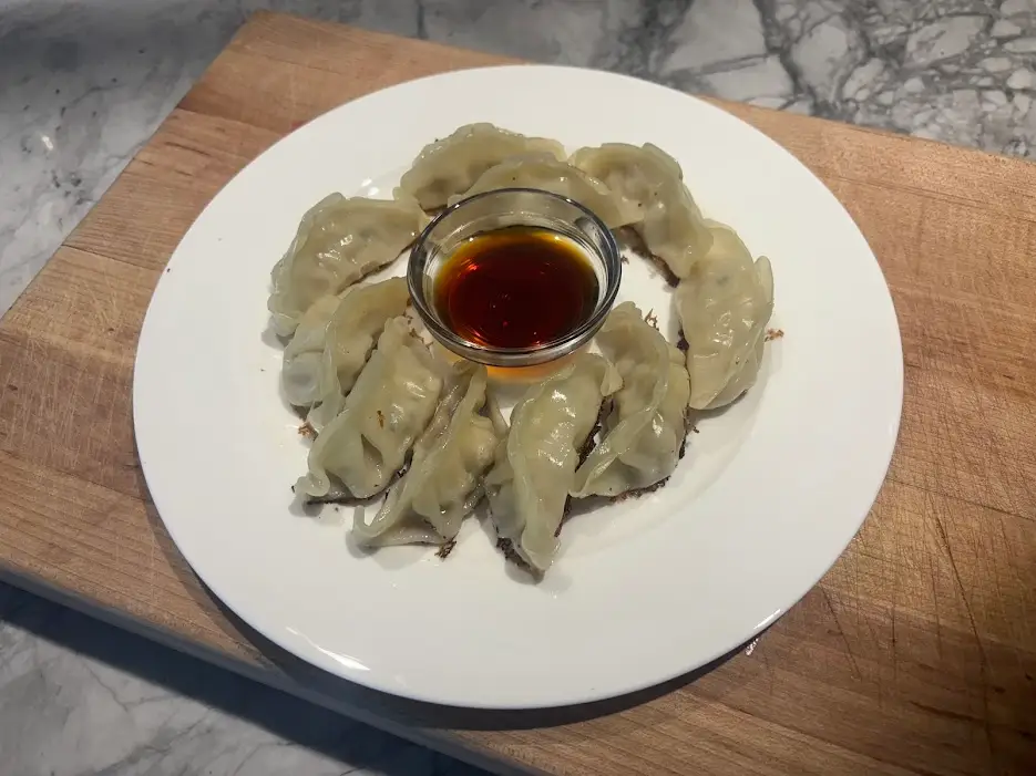 Gyoza arranged on plate around bowl with brown dipping sauce in it