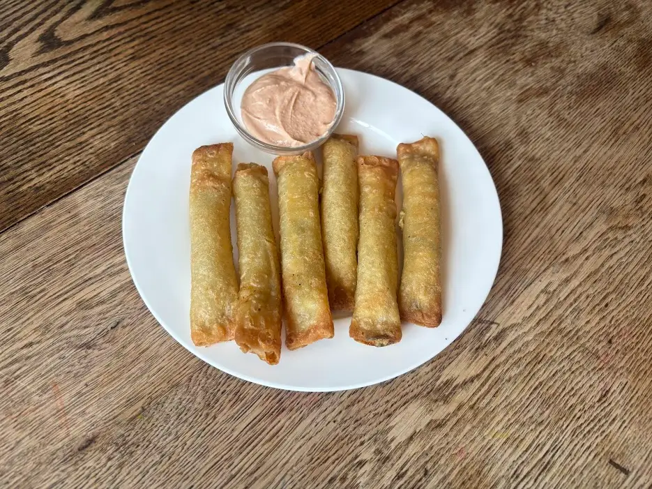 Plate of golden-brown fried firecreackers with orange dipping sauce