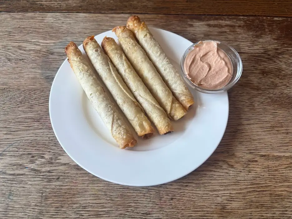 Taquitos on plate next to bowl of light orange dipping sauce