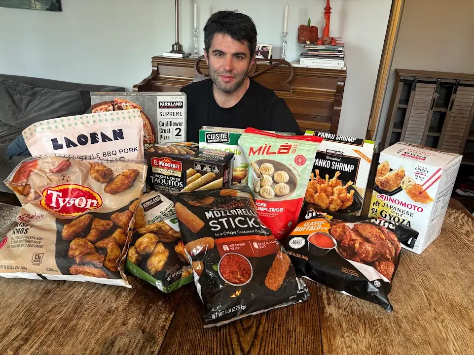 Author Ted Berg sitting behind array of appetizers from Costco arranged on wood table