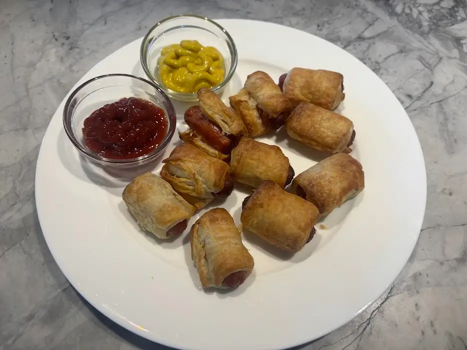 Pigs in a blanket on plate with ketchup and mustard in small bowls