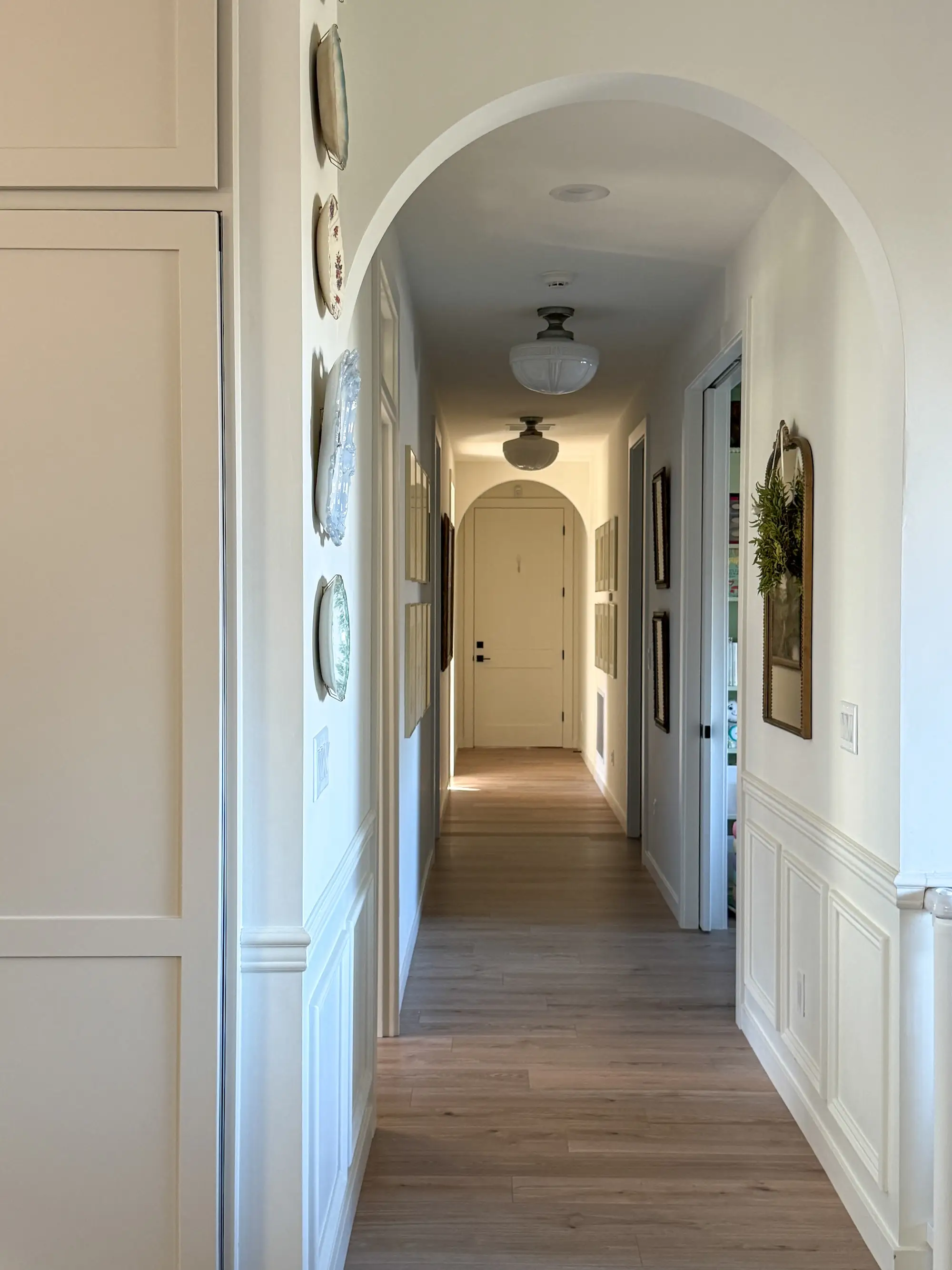 A hallway with arches and paintings on the wall that lead to a door.