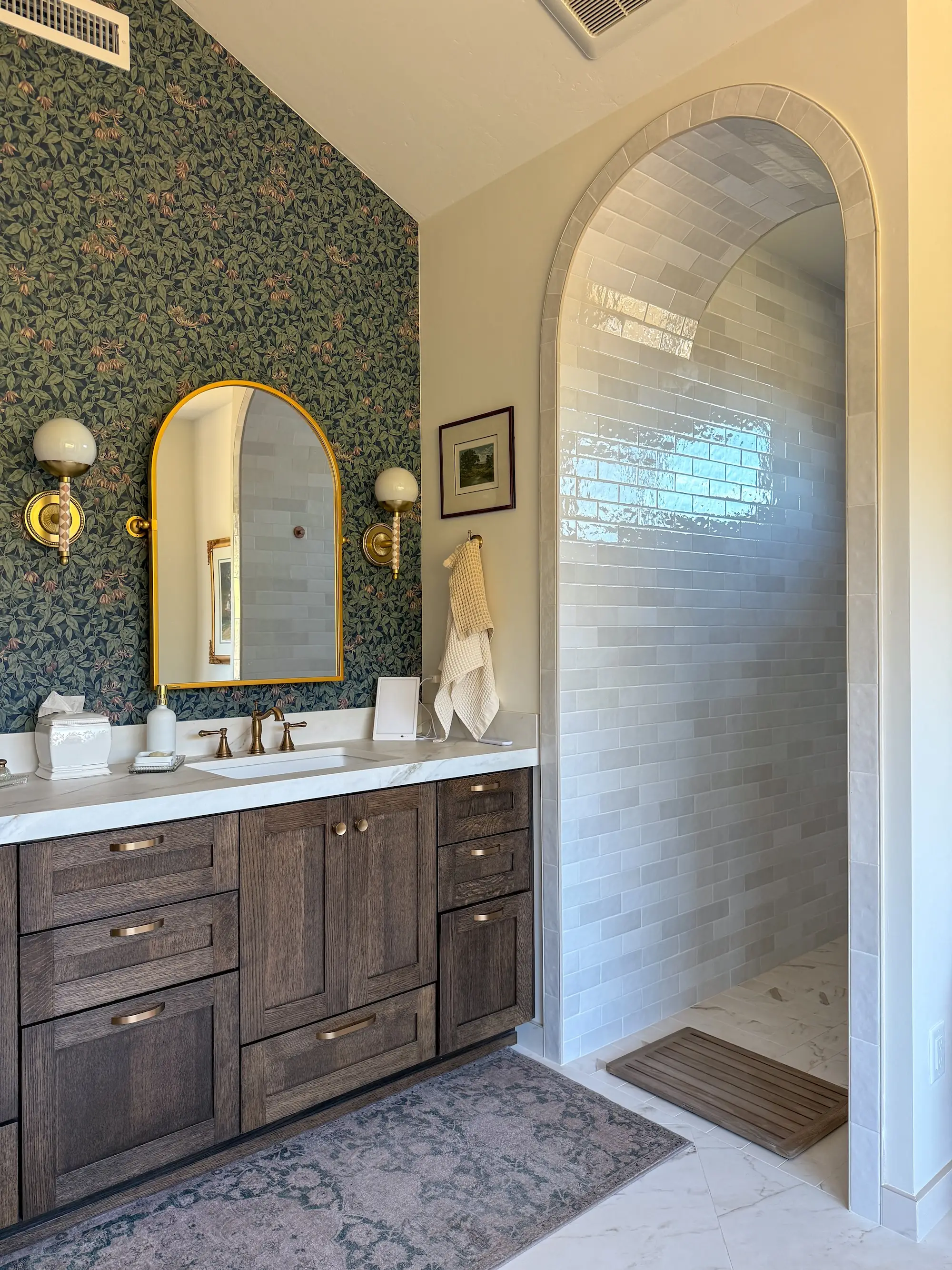 A bathroom with a green, floral wallpaper and an arched shower.
