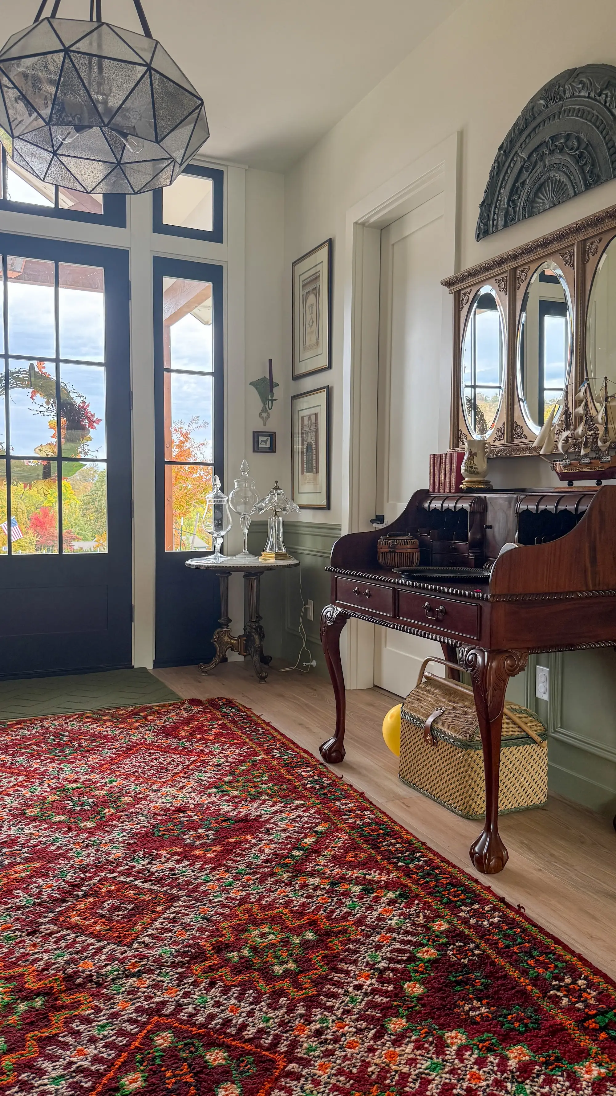 An entryway into a home with a rug, antique desk, and large chandelier.