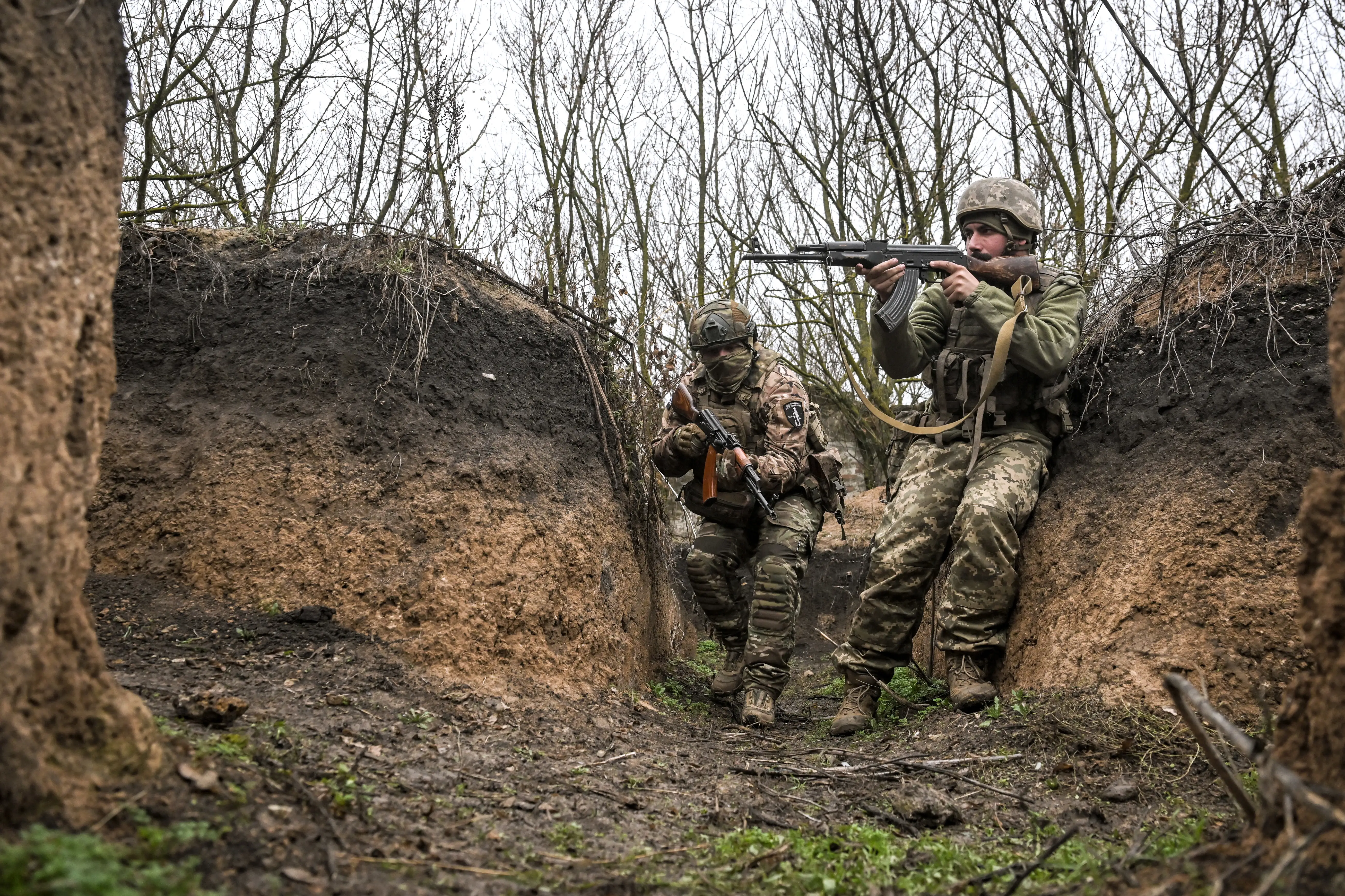Two men in a trench holding firearms on a grey day.