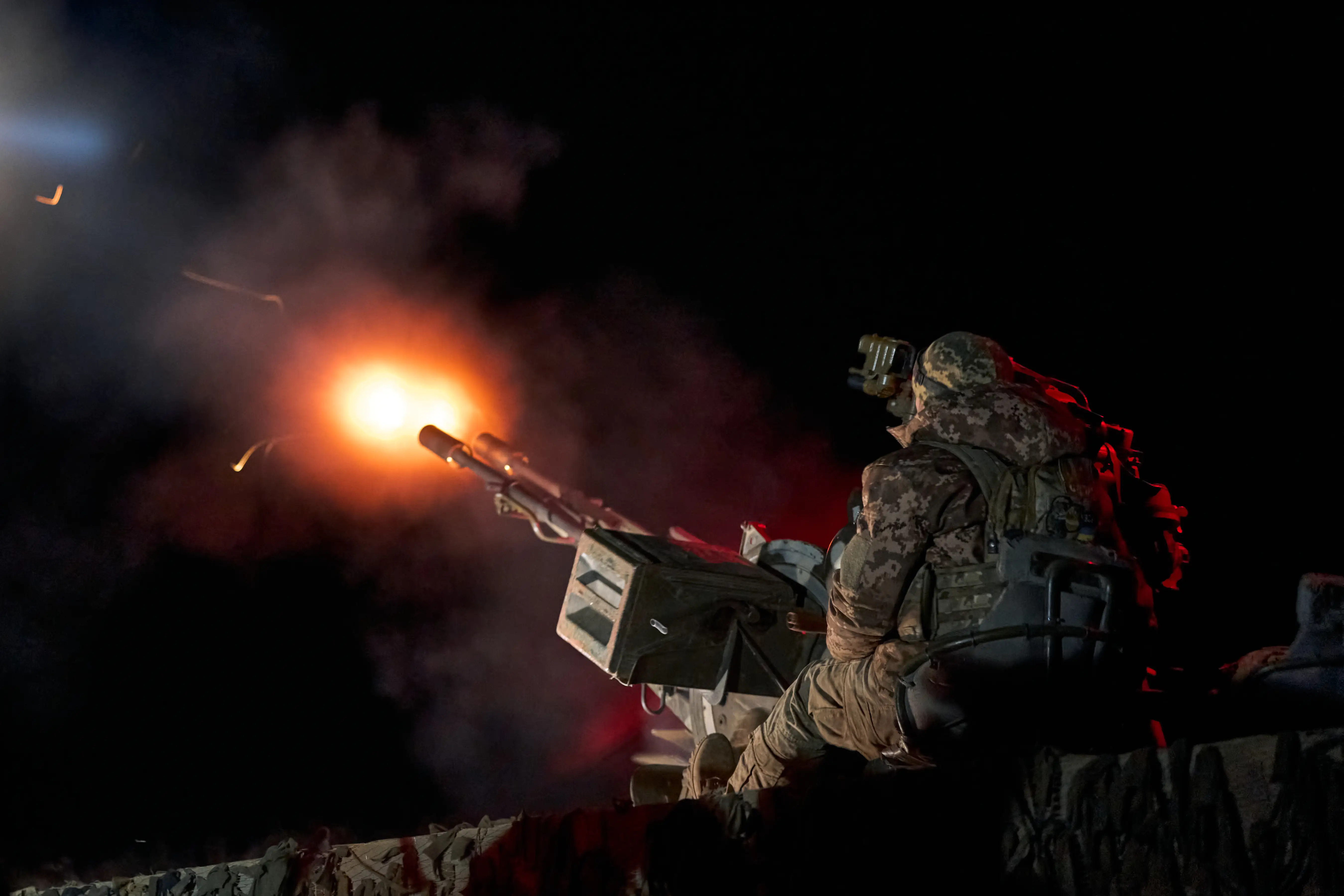 A person in camouflage gear fires a piece of weaponry into a black sky