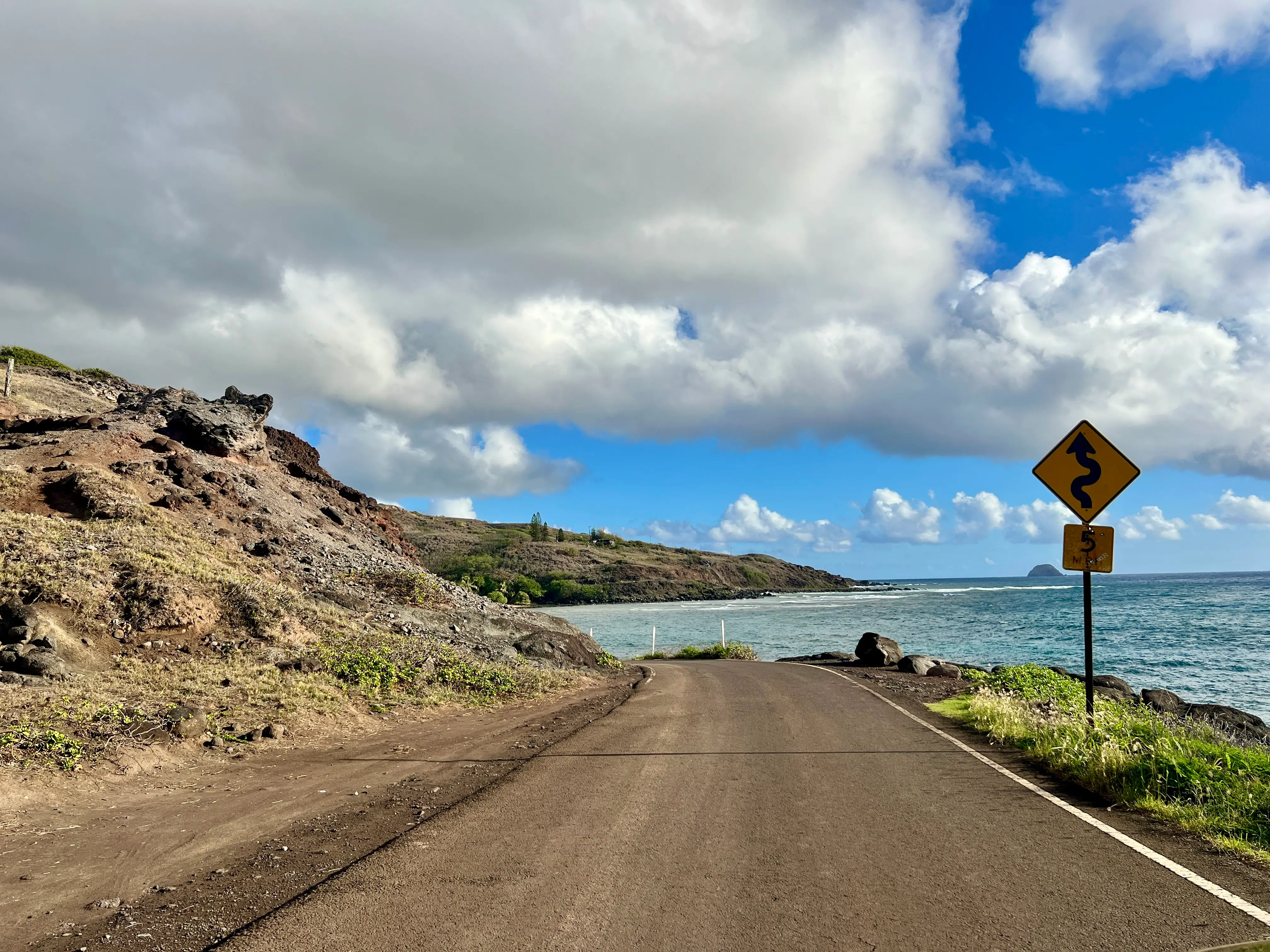 Road with mountains on one side, water on the other and winding road sign, 5 mph