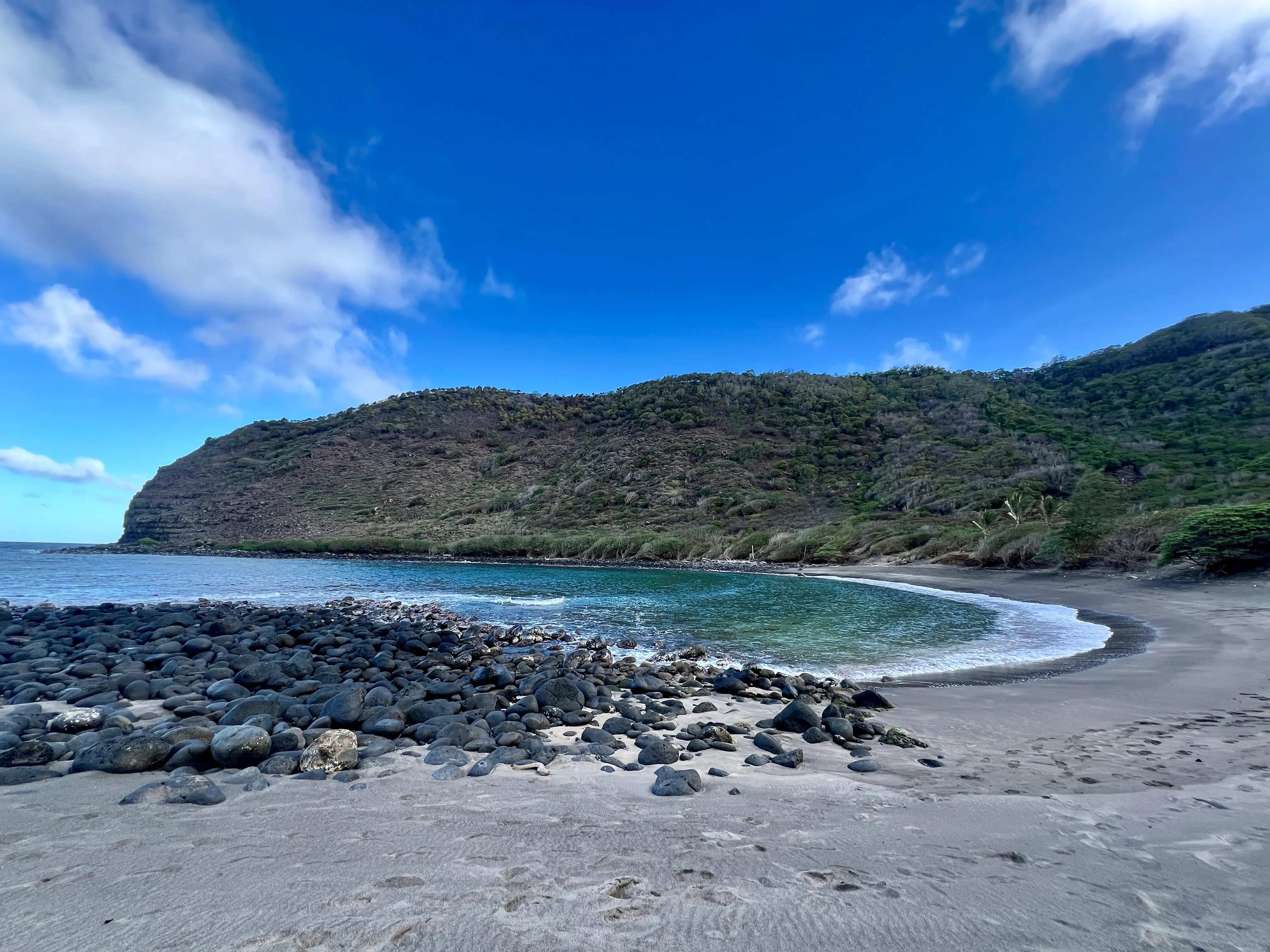 Beach in Molokai with stones along shore, hills in background